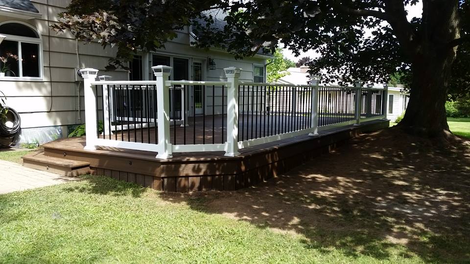 A long, narrow deck connected to a house and shaded by a large tree.