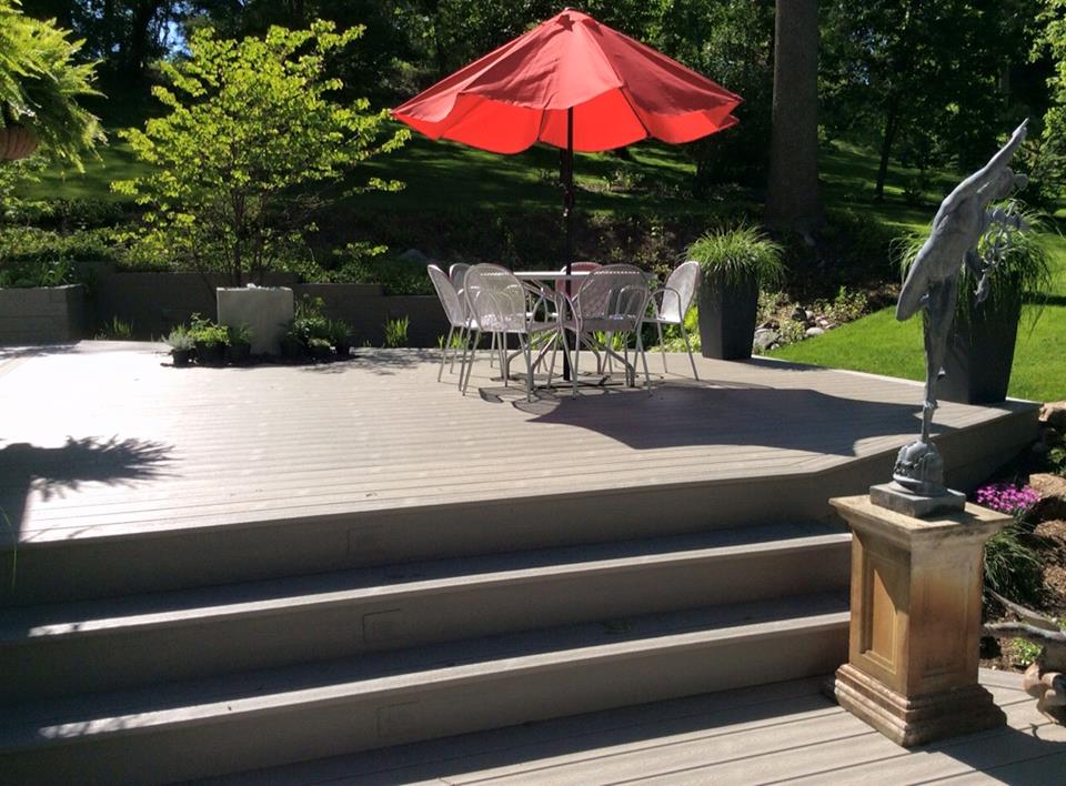 A curved deck with a patio table and chairs set and a bright red patio umbrella.