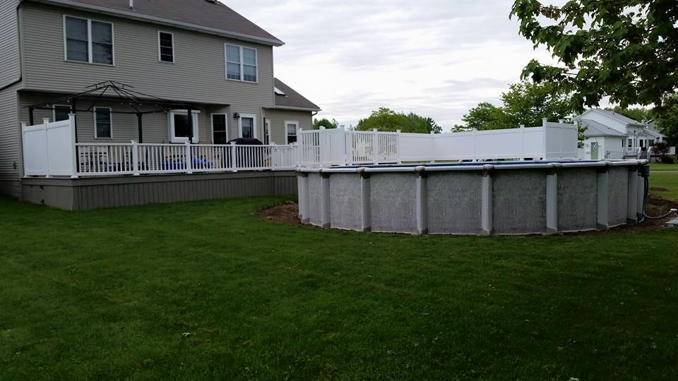 A large deck lined with white fencing that connects to an above-ground pool.
