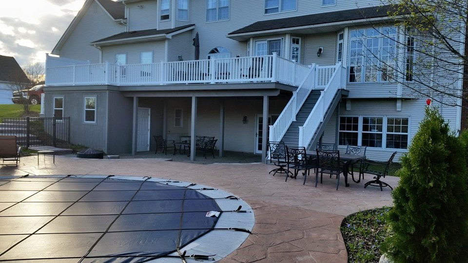 A large, second story deck with stairs leading down to the first story deck surrounding an in-ground pool.