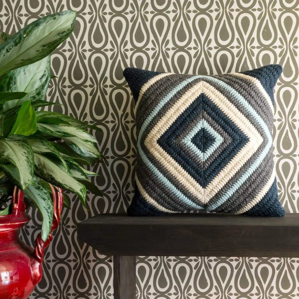 Handmade textured navy blue diamond throw pillow shown with gray block printed wallpaper.
