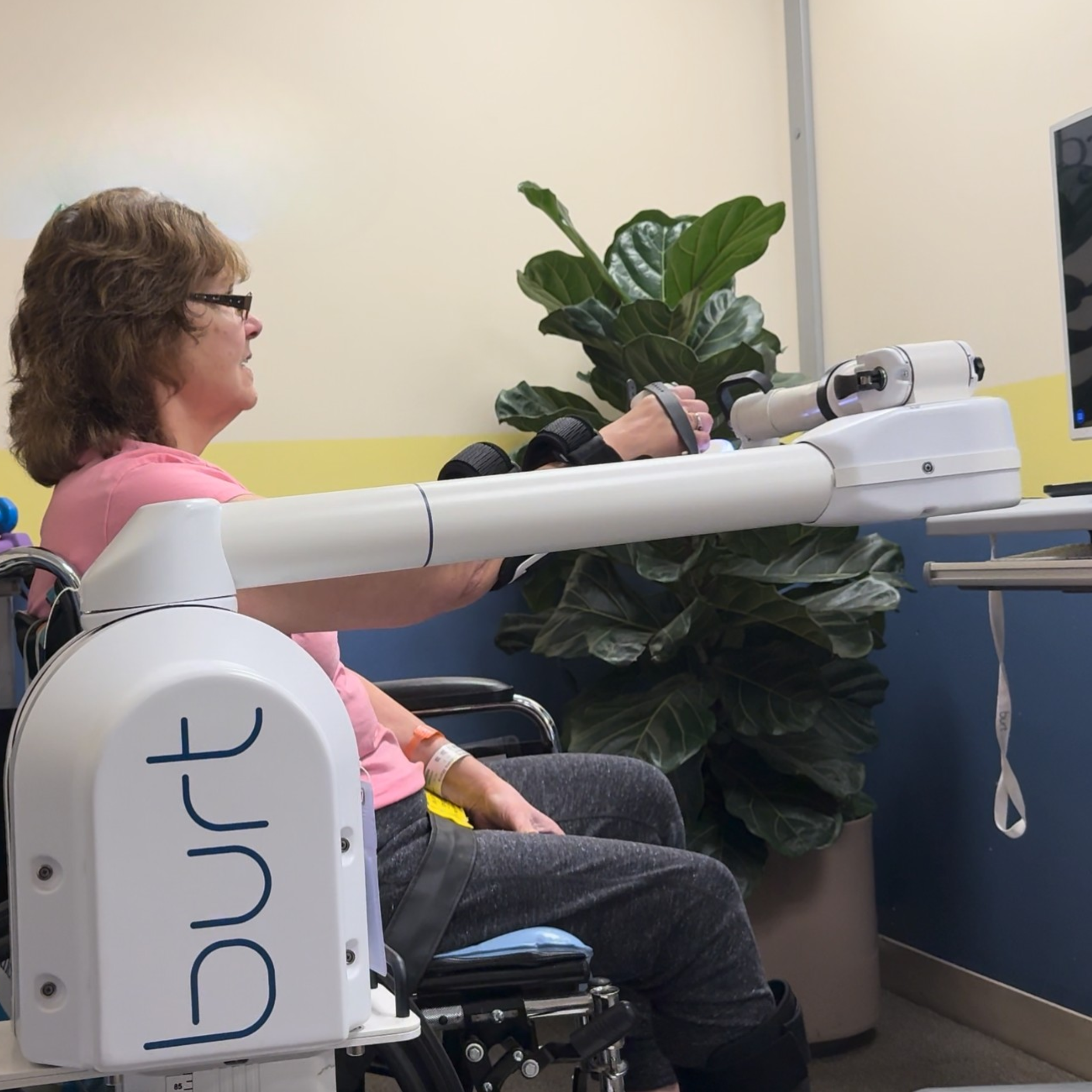 Woman in a wheelchair using a robotic arm to interact with a computer monitor.