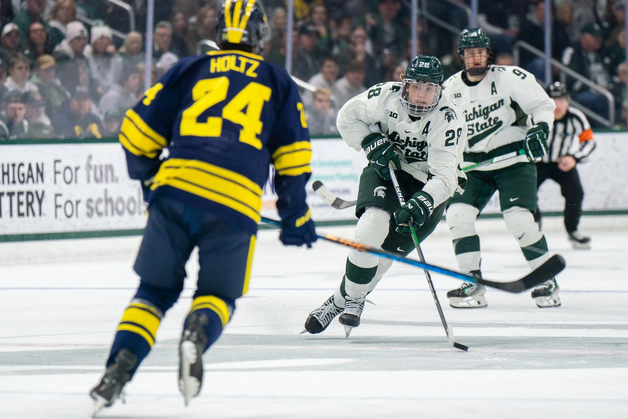 Michigan State forward Karsen Dorwart (28) carries the puck up the ice towards Michigan defenseman Steve Holtz (24) during the Big Ten Hockey Tournament championship game at Munn Ice Arena in East Lansing, Mich., Saturday, March 23, 2024.