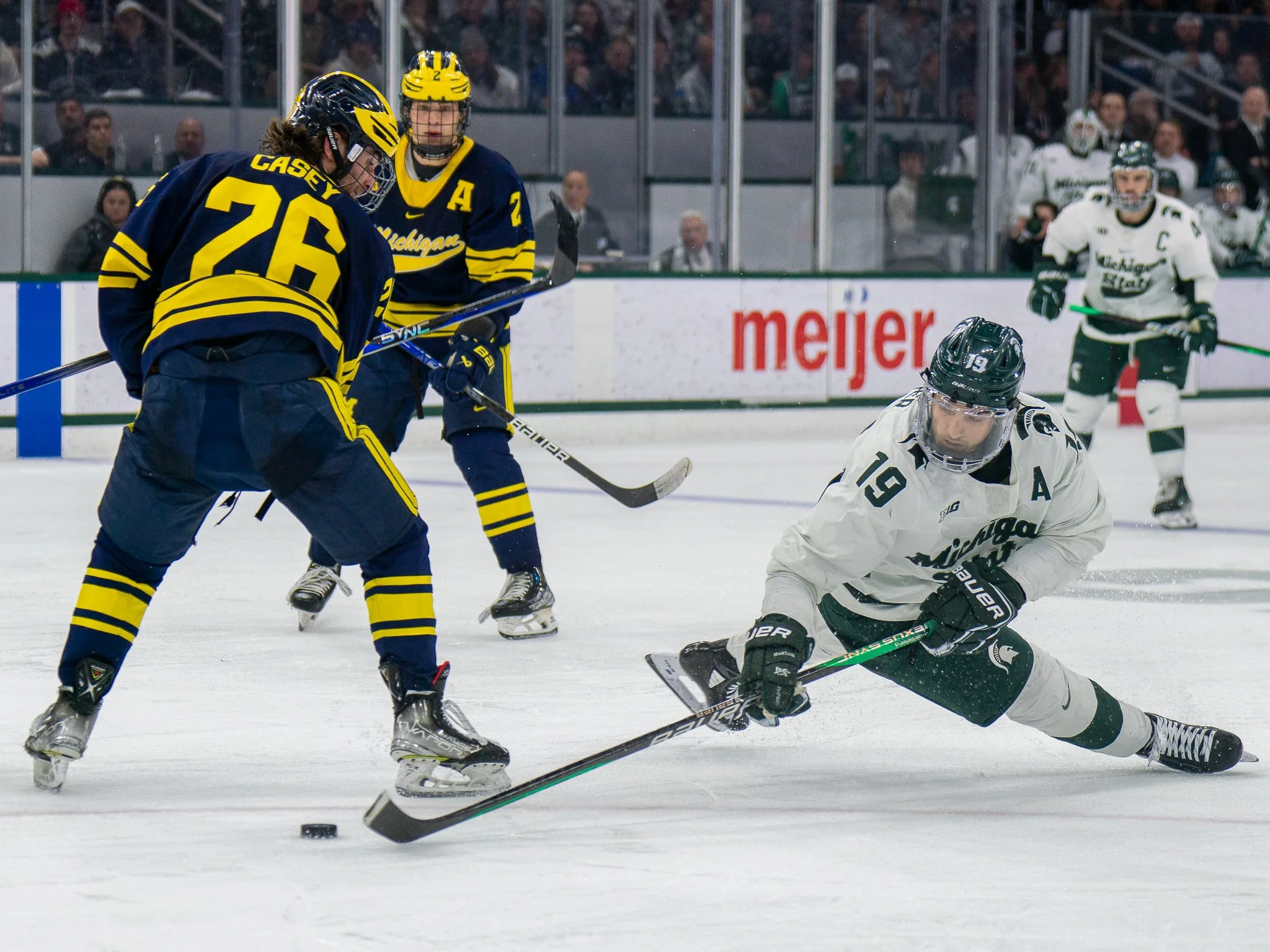 
Michigan State forward Nicolas Müller (19) completes a pass while falling to the ice as Michigan defenseman Seamus Casey (26) looks on during the Big Ten Hockey Tournament championship game at Munn Ice Arena in East Lansing, Mich., Saturday, March 2