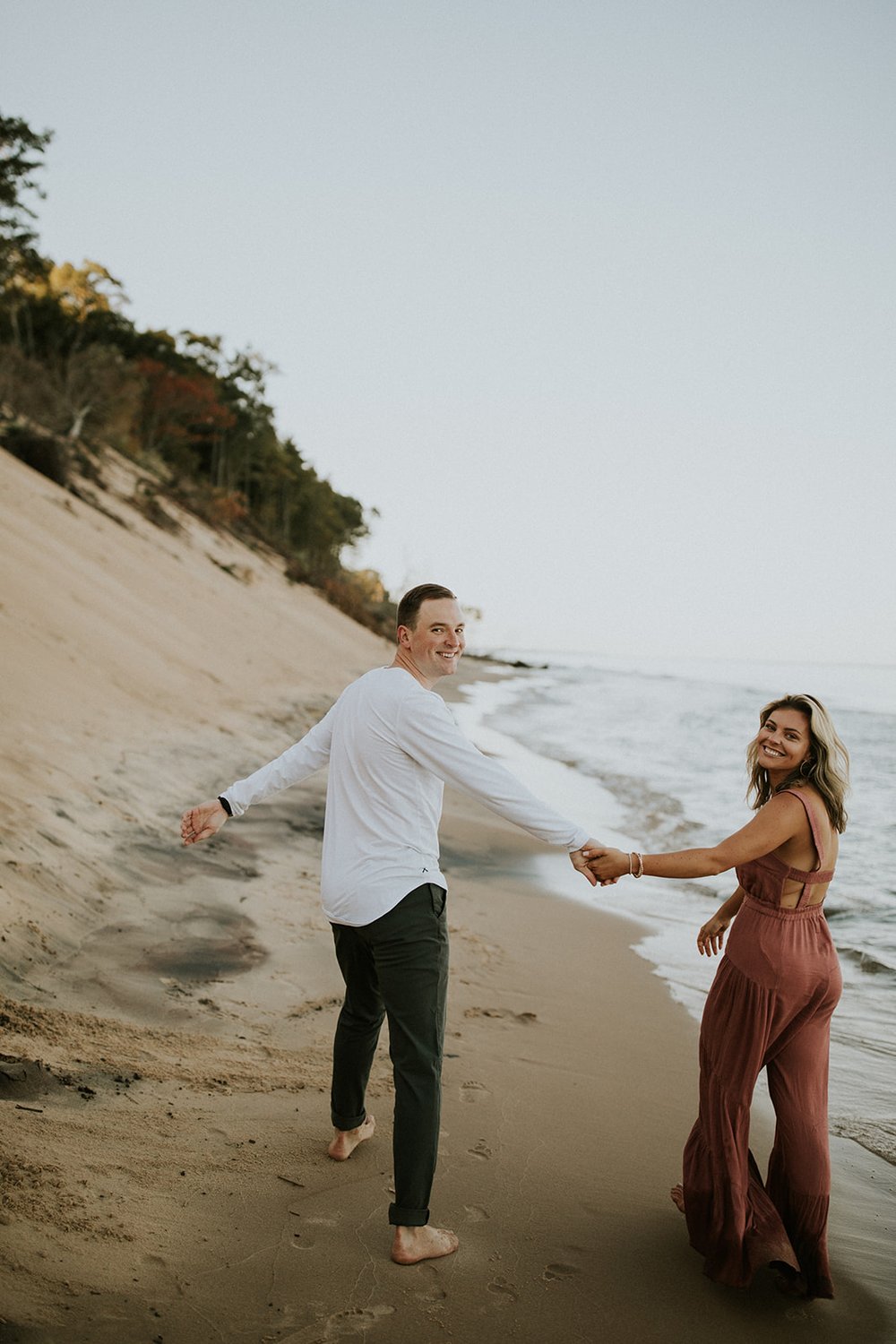 Couple walks down the beach in their coordinating, neutral engagement photos outfits 