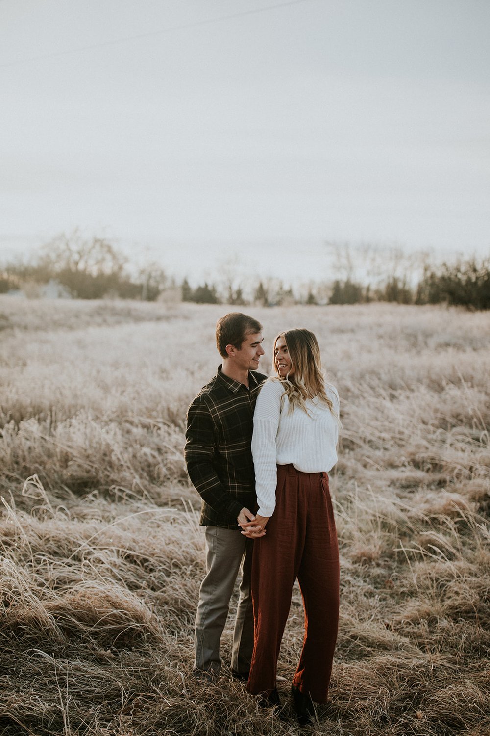  Couple in a field for engagement photos, an example of what to wear that includes neutral colors and seasonally appropriate outfits. 