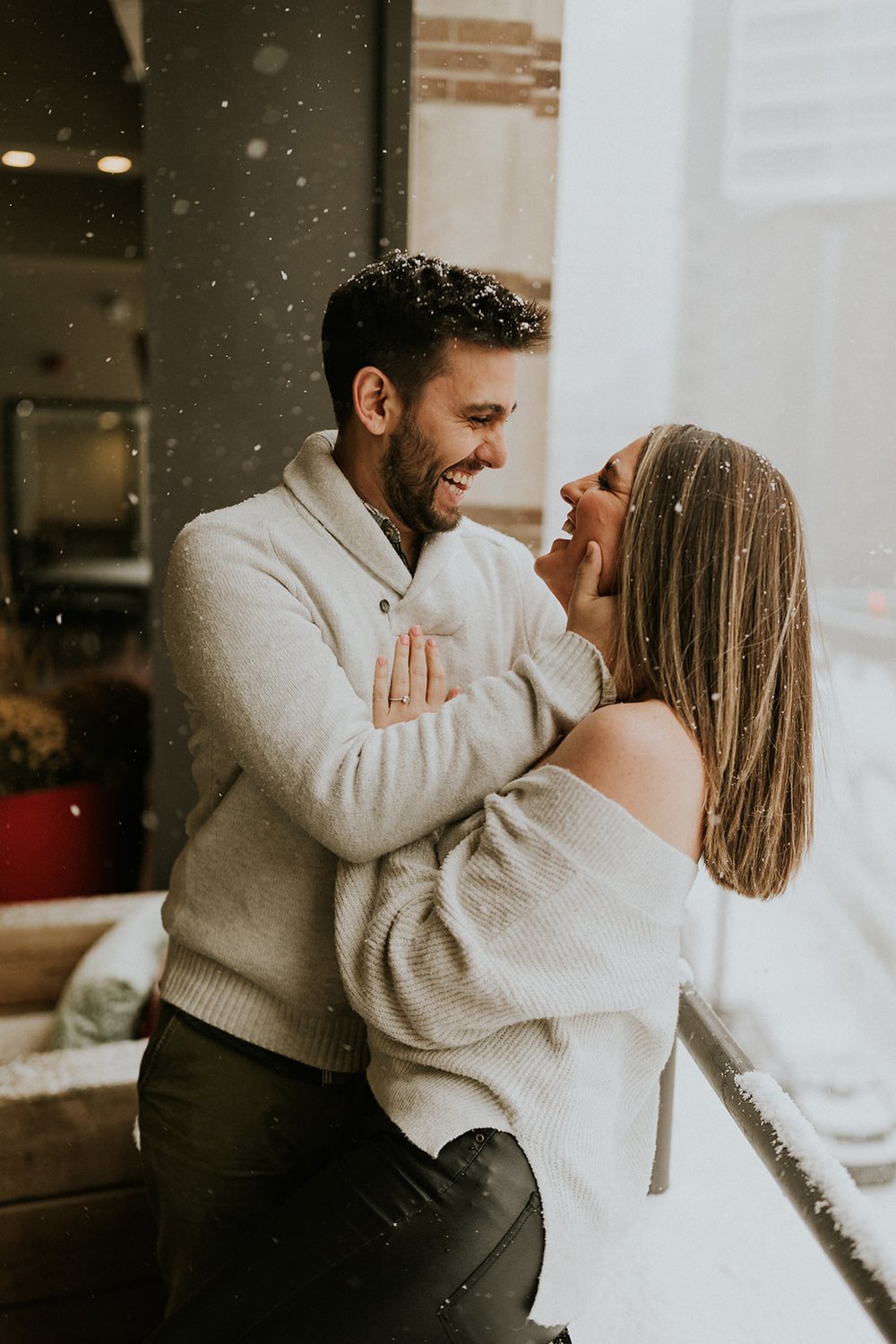  Couple embraces in the snow, wearing warm white sweaters. 