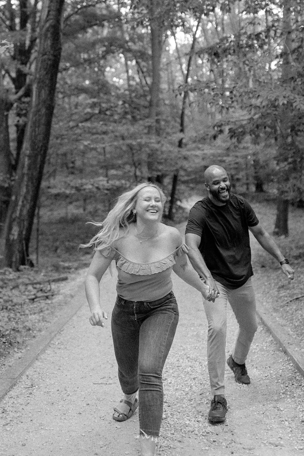  engaged couple running and laughing on path at Grand Haven Engagement session 