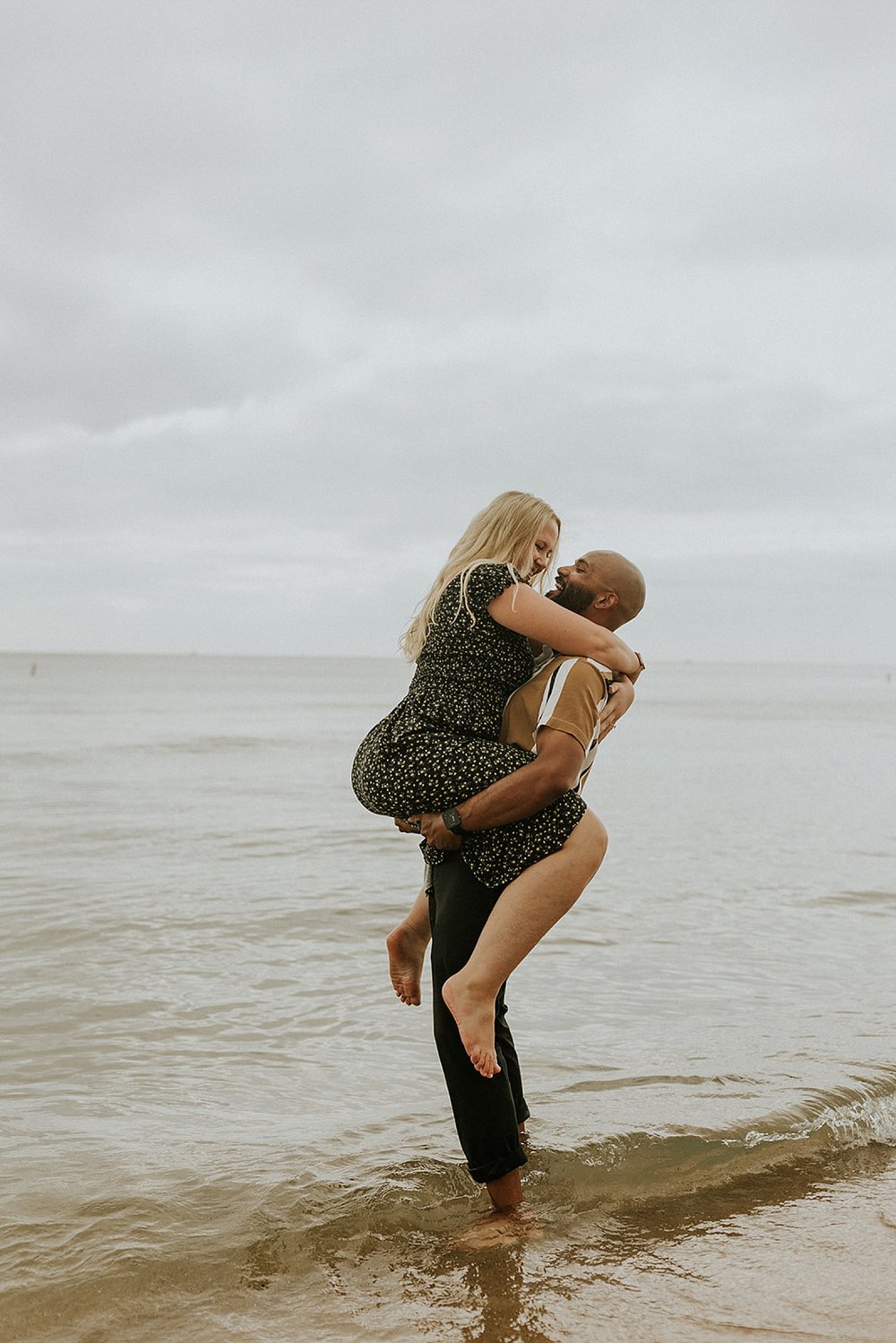  blonde woman being held up by fiance at Grand Haven Engagement session 
