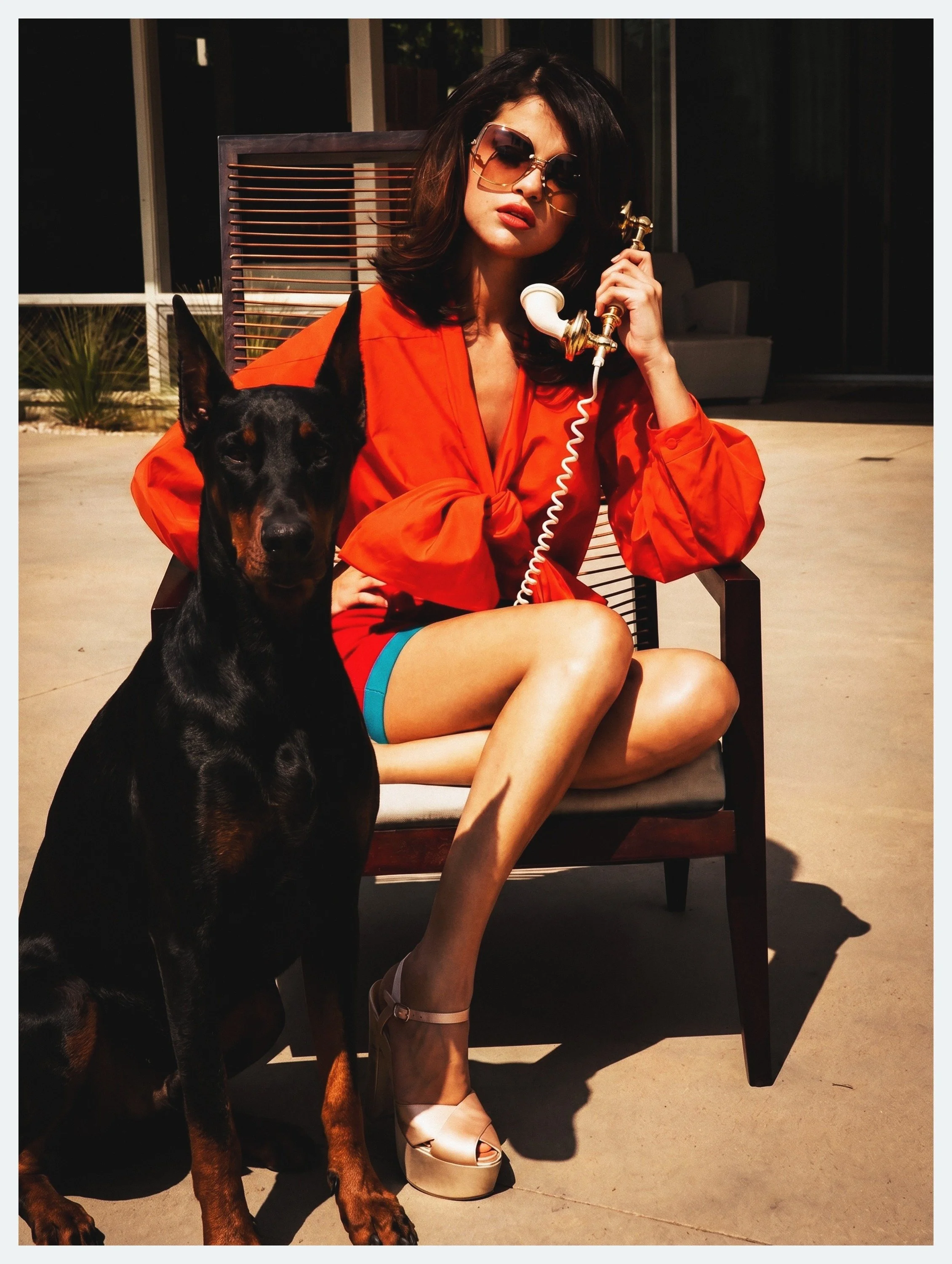 Selena Gomez in sunglasses and an orange blouse beside a Doberman for Elle México, by celebrity photographer Steven Gomillion