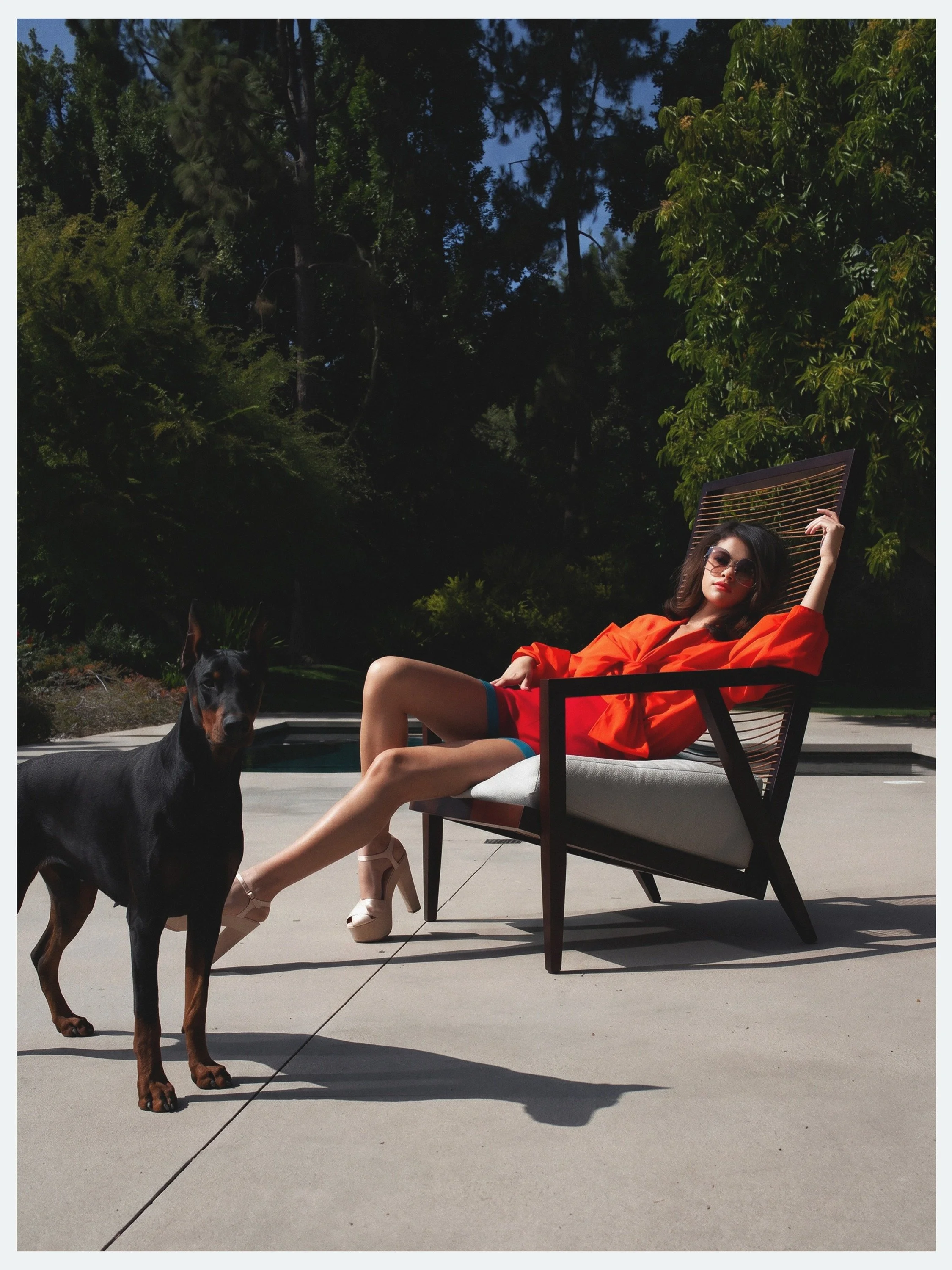 Selena Gomez in an orange blouse on a poolside lounge chair with a Doberman for Elle México, by celebrity photographer Steven Gomillion