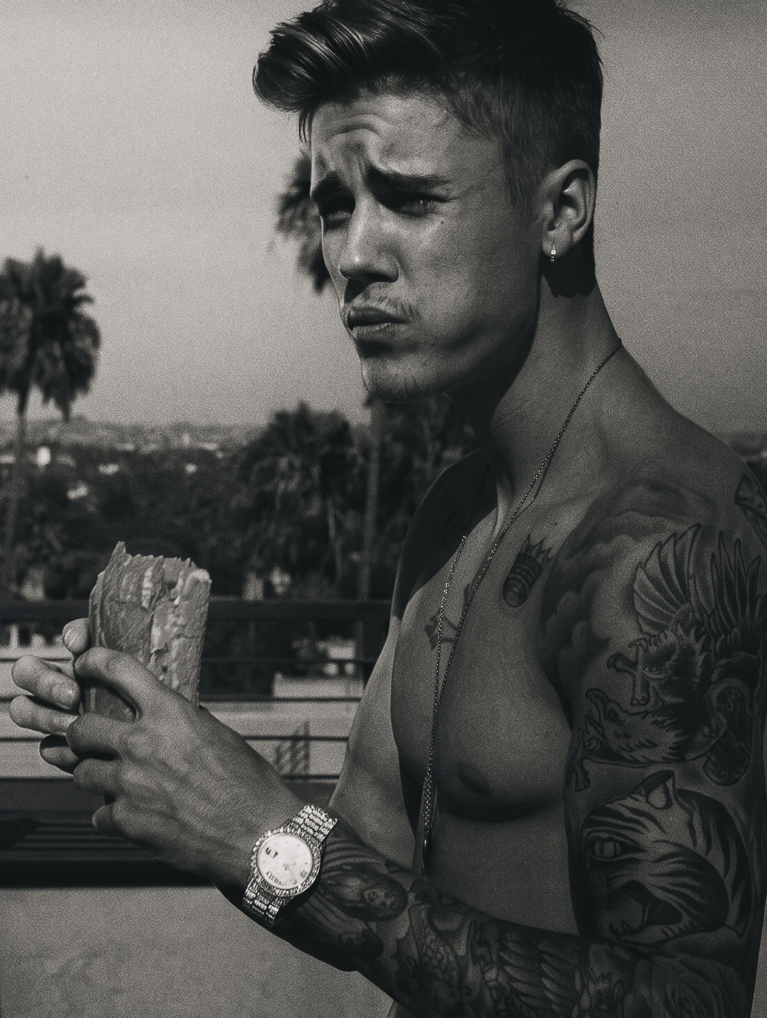 Justin Bieber by celebrity photographer Steven Gomillion. Shirtless on the rooftop holding a sandwich, his tattoos, chain and diamond watch in sharp detail, with palm trees behind. Black and white, slightly warm silver tone with soft grain.