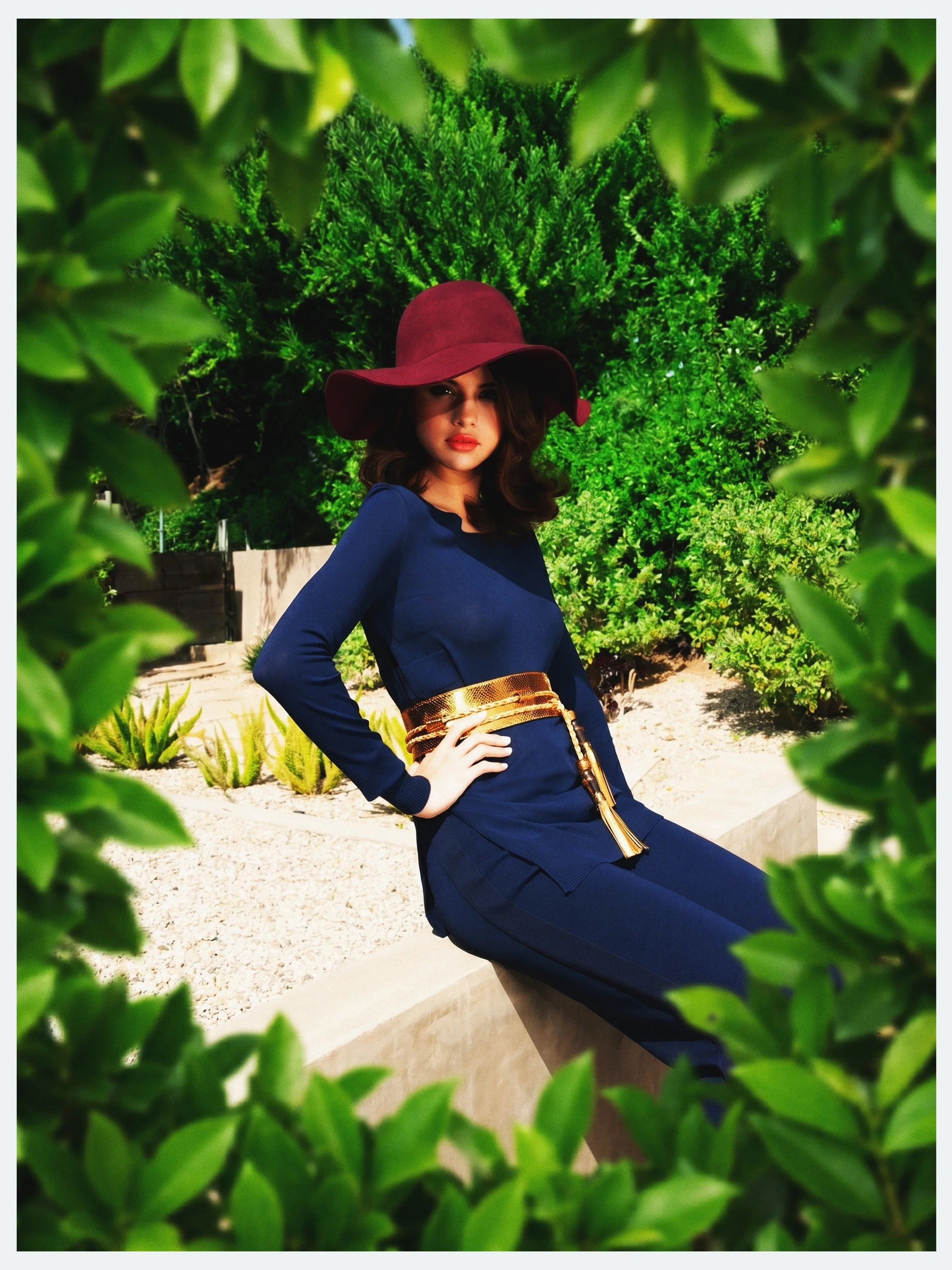 Selena Gomez in a wide-brim hat seen through green leaves for her Elle México cover story by celebrity photographer Steven Gomillion