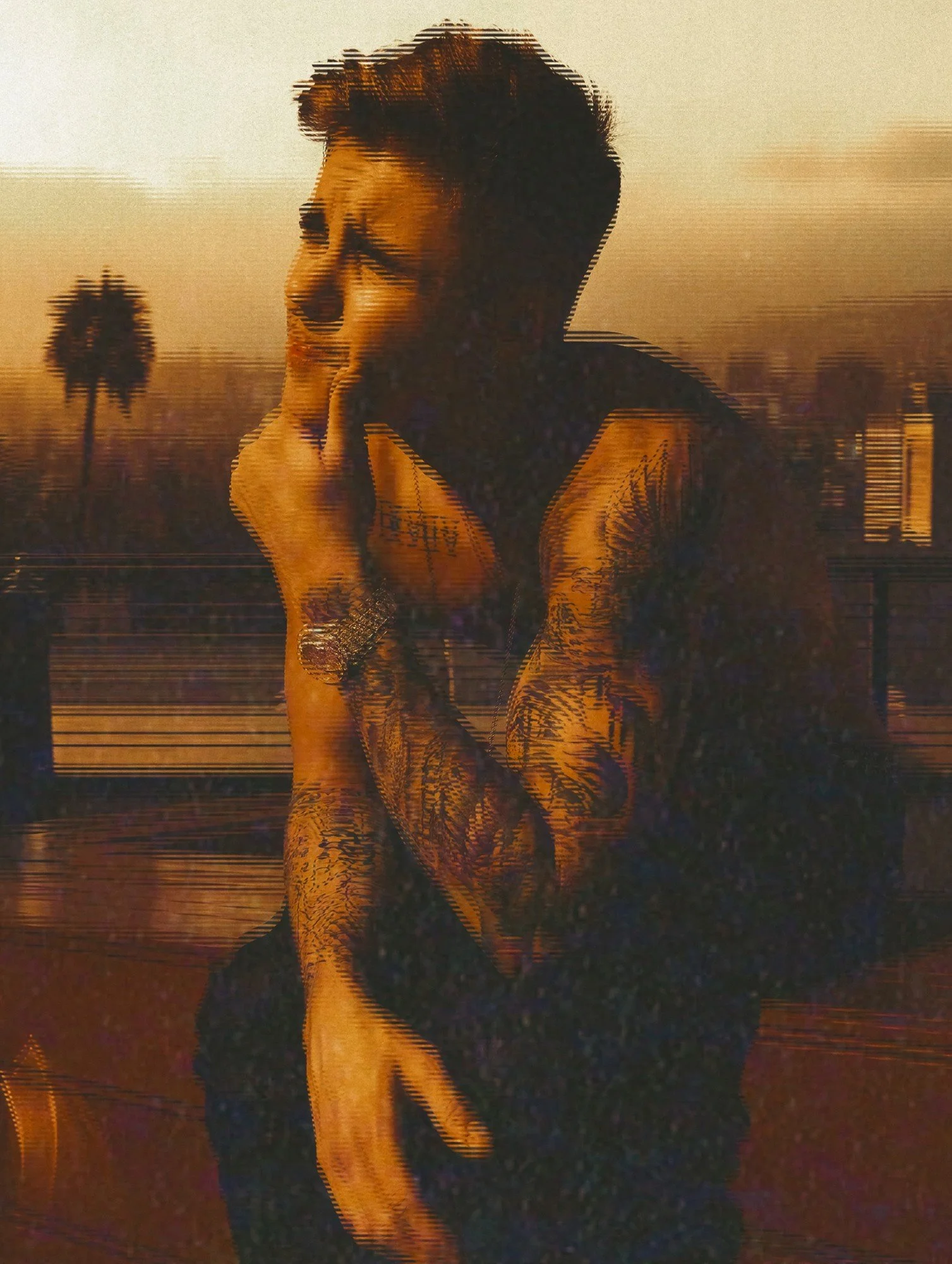 Justin Bieber by celebrity photographer Steven Gomillion. Shirtless with heavily tattooed arms, he raises a hand to his mouth on the rooftop, with a palm tree silhouetted against a hazy skyline. Heavy grain and horizontal glitch distortion over a war