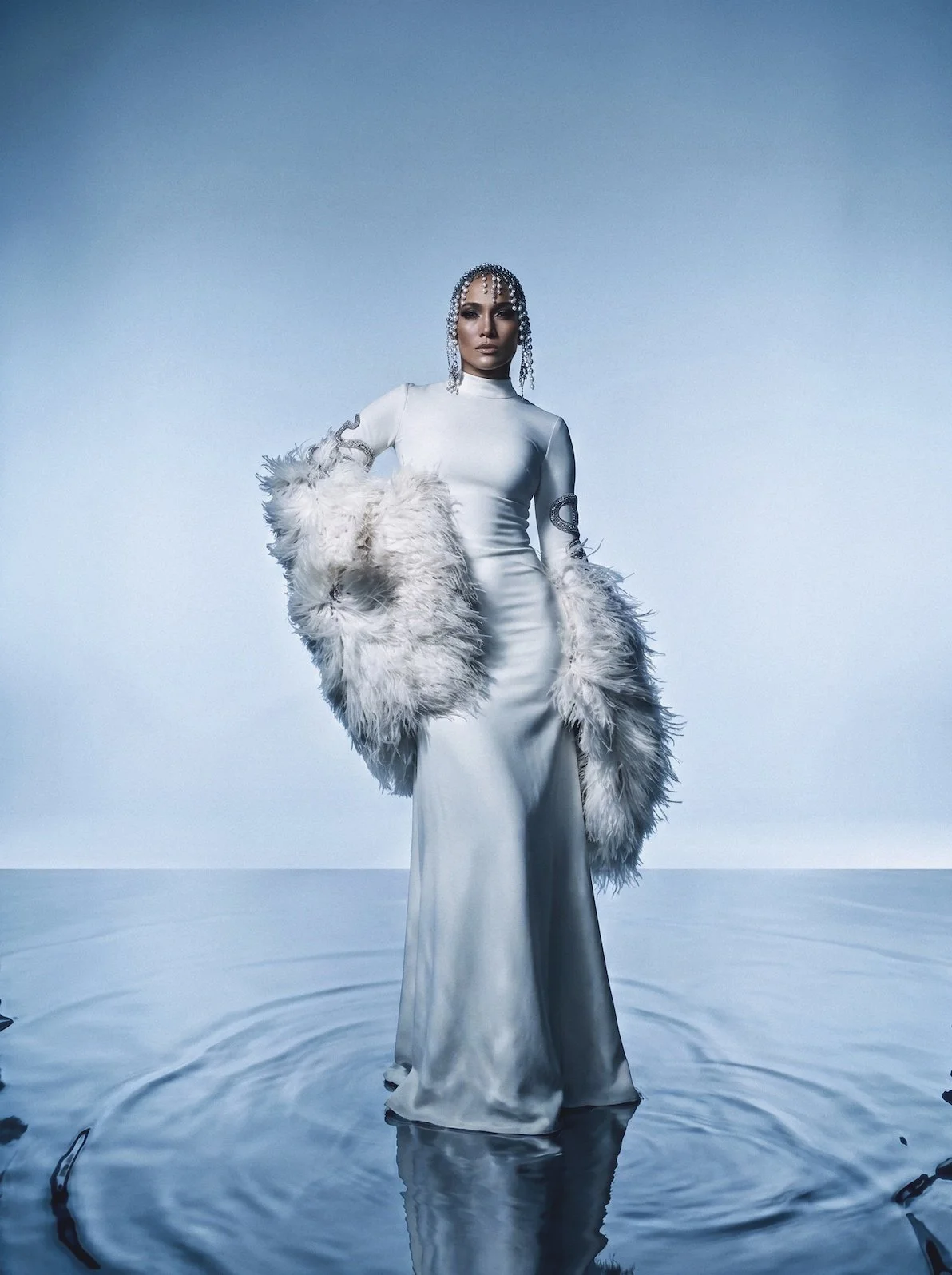 Jennifer Lopez in a white gown with feather sleeves and a crystal headpiece standing on water by celebrity photographer Steven Gomillion