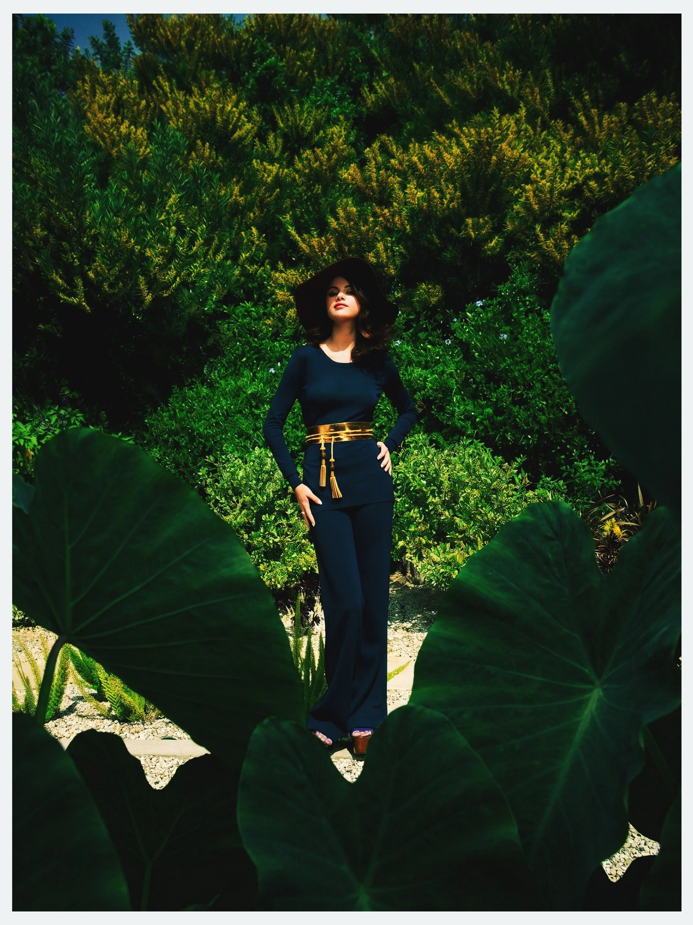 Selena Gomez in a black wide-brim hat among giant garden leaves for Elle México, by celebrity photographer Steven Gomillion