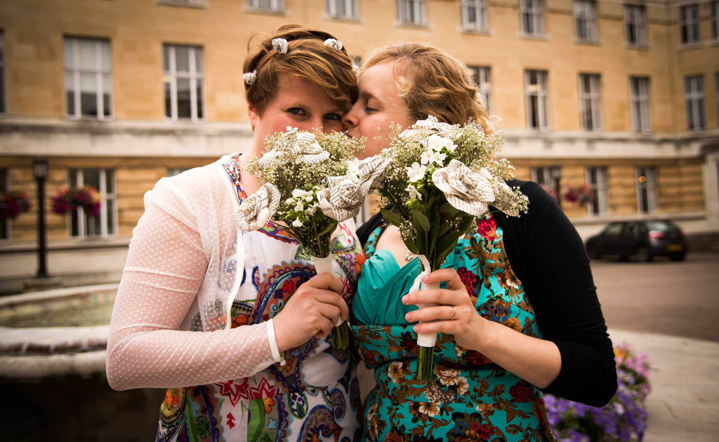 Two women kissing with their paper flower bouquets outside Wandsworth Town Hall after being married.