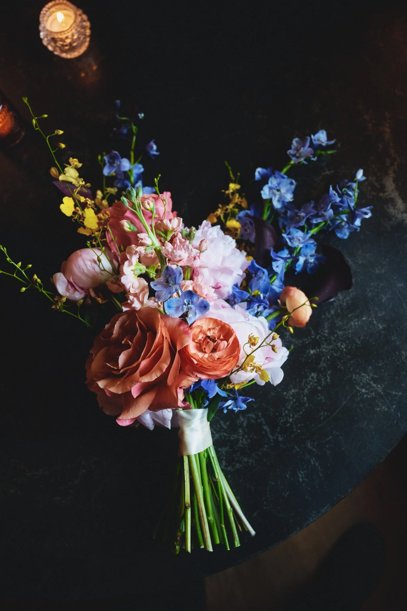  A bridal bouquet of garden roses, delphinium and orchids on a dark table at Il Mercato in New Orleans 