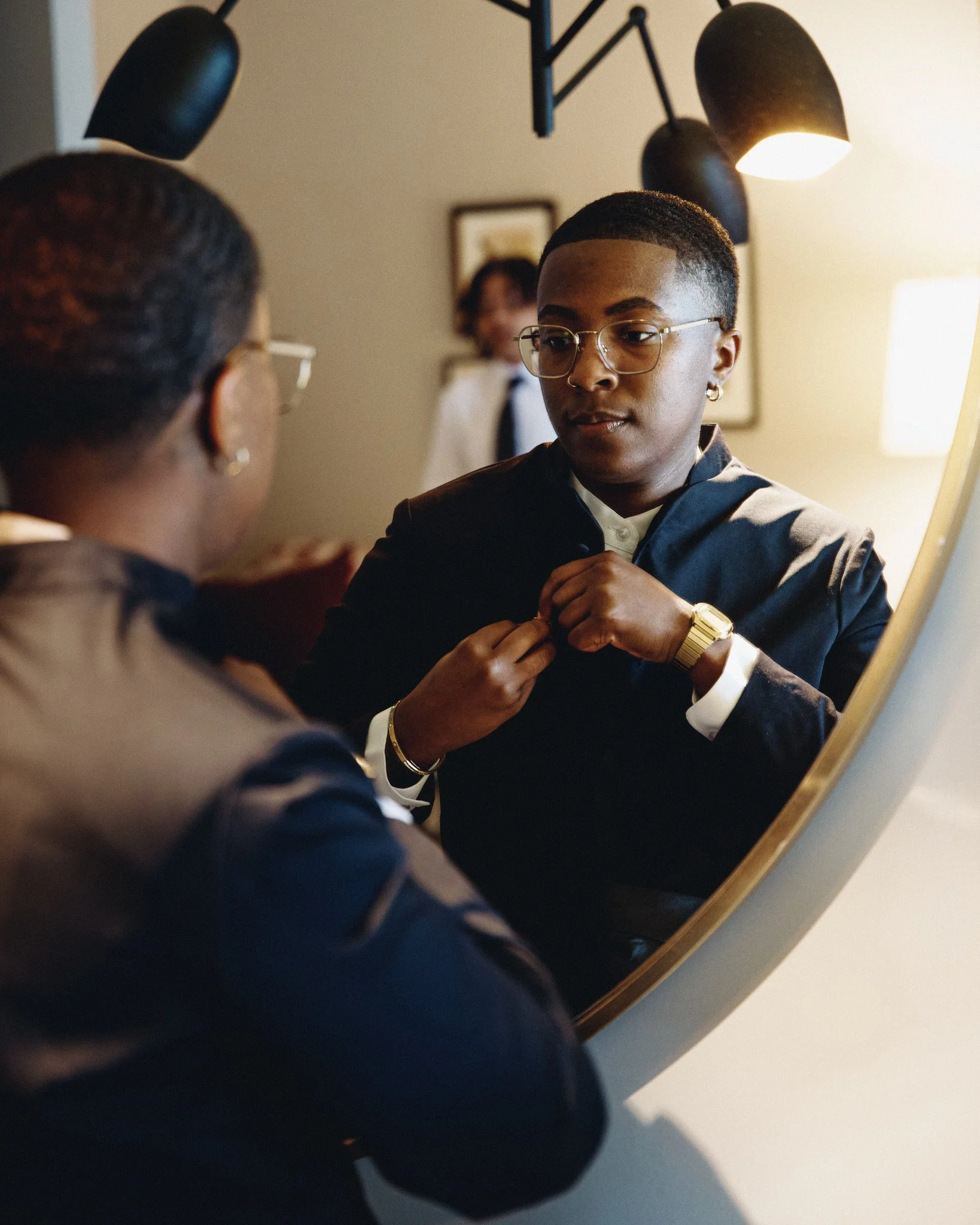  A partner having their collar adjusted in a round mirror before the ceremony 