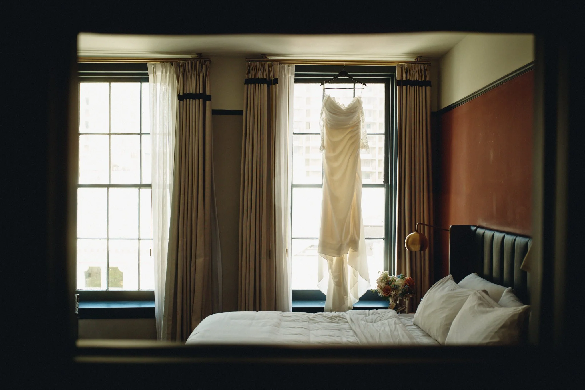  A wedding dress hanging in the window, reflected in the mirror of the getting-ready room 
