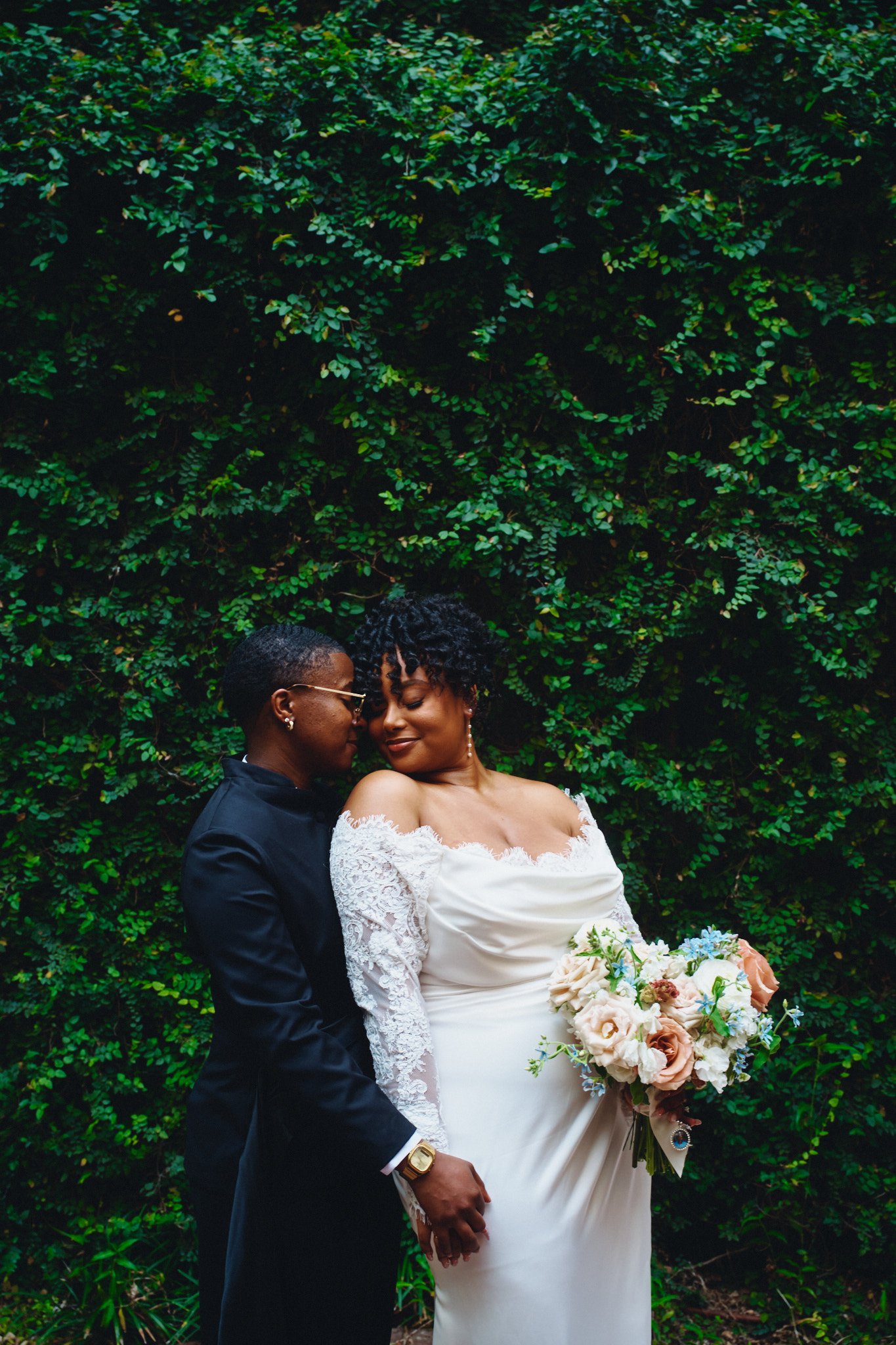  A couple embracing in front of a wall of greenery before the ceremony 