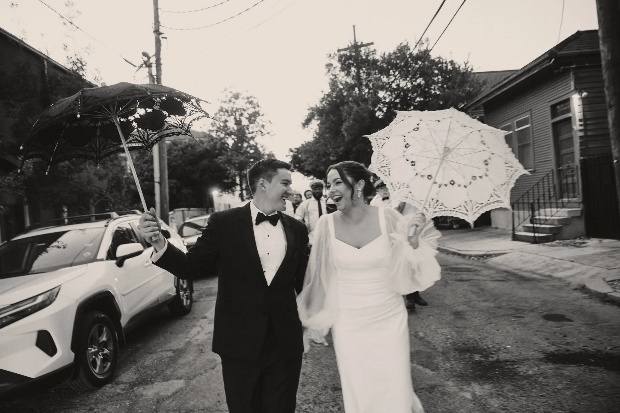  A bride and groom laughing under lace parasols during their second line outside Capulet in New Orleans 