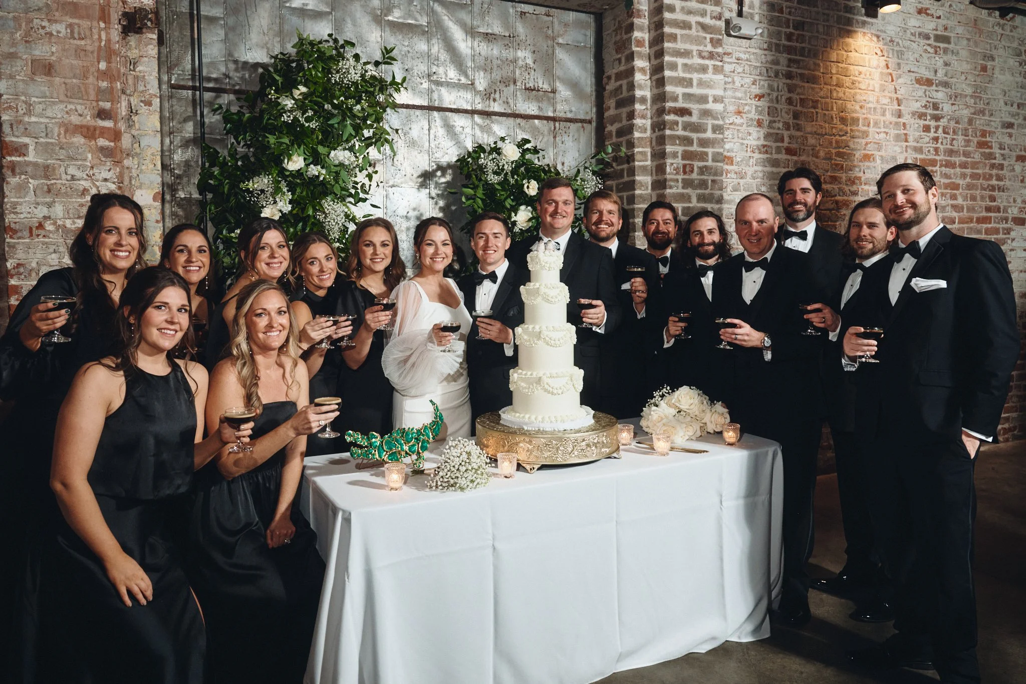  The wedding party raising a toast around the cake against the brick wall at Capulet in New Orleans 