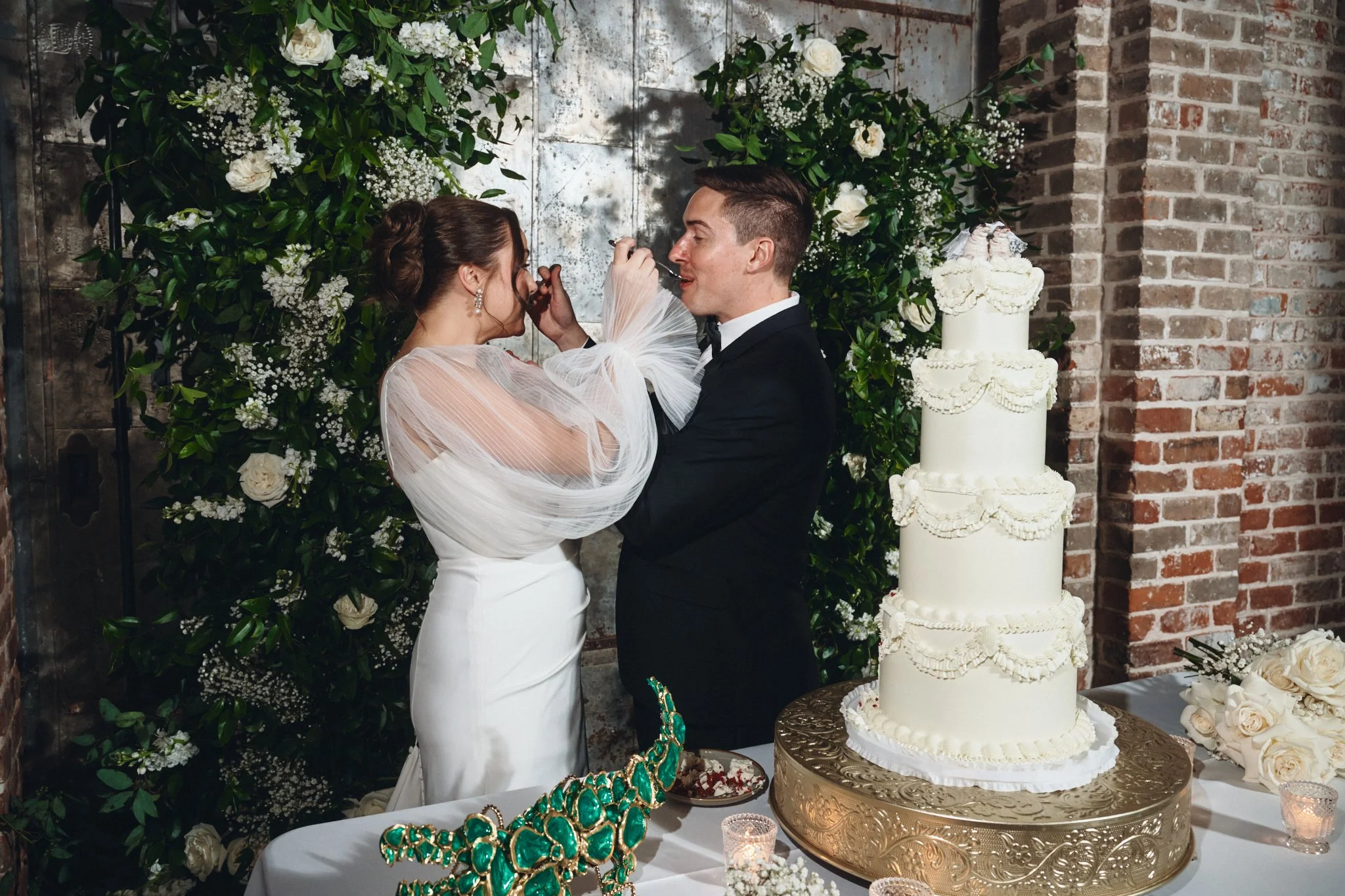  A bride and groom feeding each other cake in front of the floral doorway at Capulet in New Orleans 