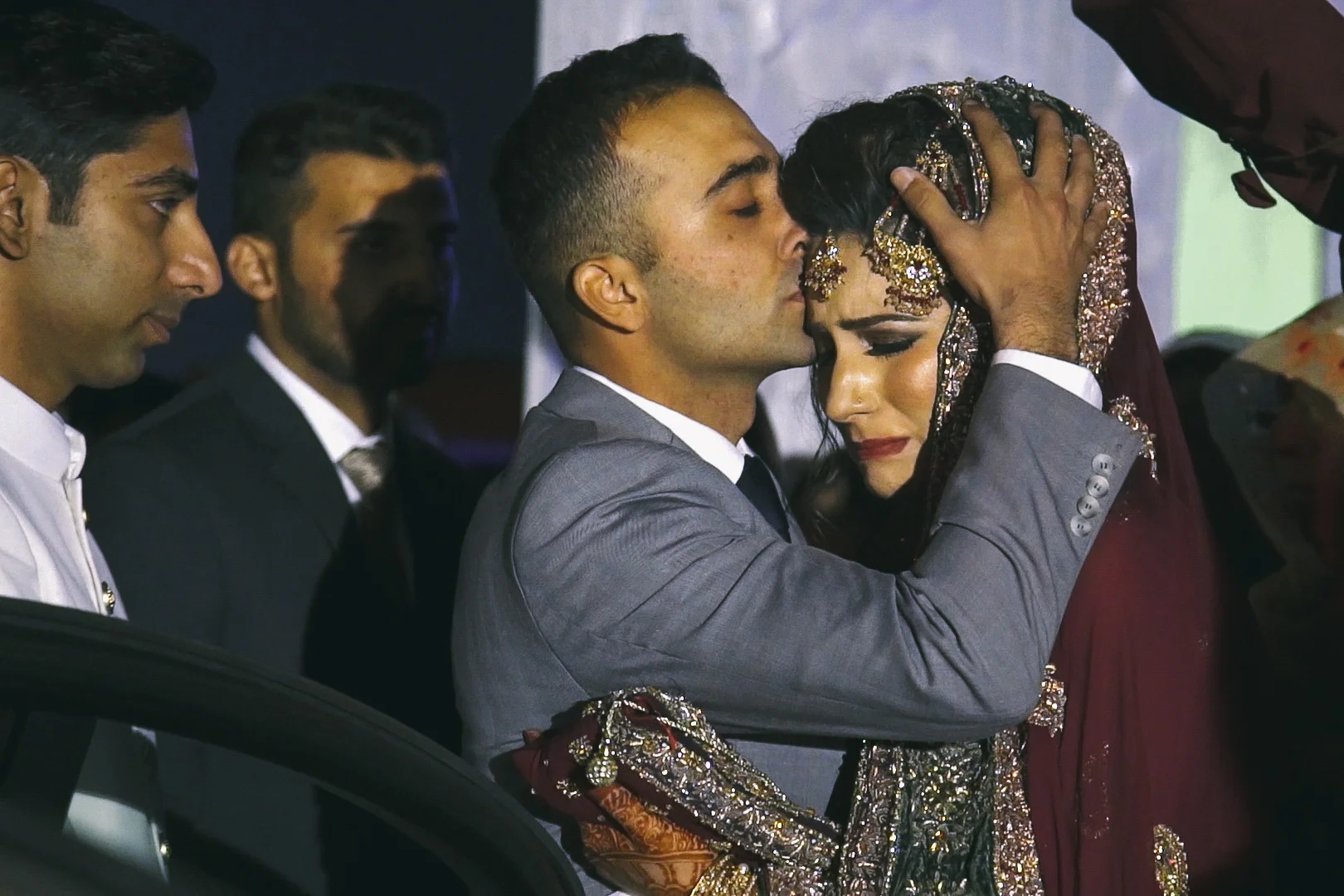 Farheen is kissed by Abdullah, her brother, as she is escorted out of the wedding venue on her baraat . Her husband, Zia (left), waits to escort her to his family's home. The baraat is a somber occasion for the bride's parents as it signifies the departure of their daughter from their home. The departure of the bride during this ceremony is a very emotional scene as she says farewell to the home of her parents and siblings to start a new married life with her husband's family.