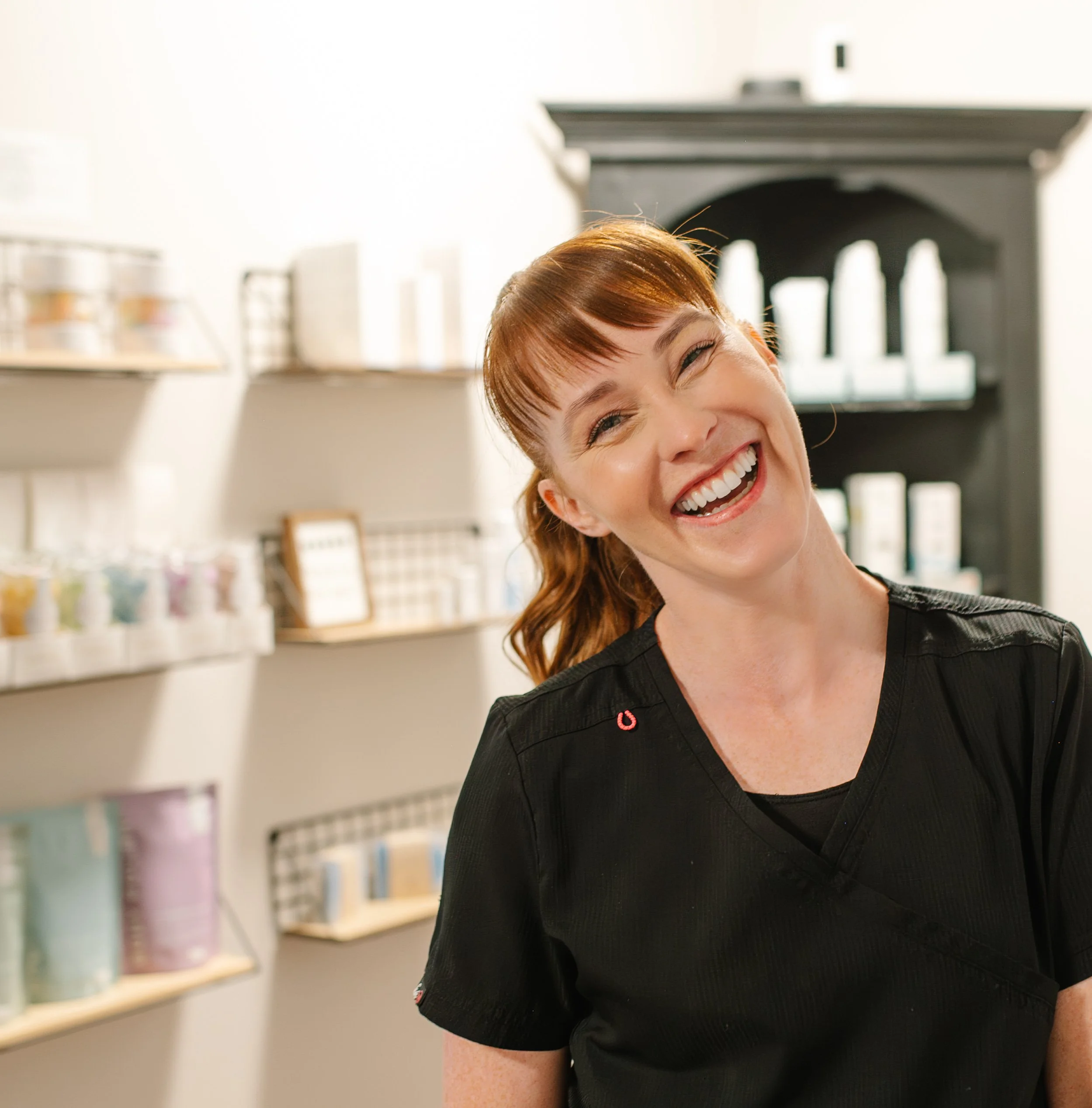 Zoey smiling beside skincare product shelves at Essential Esthetics by Zoey.