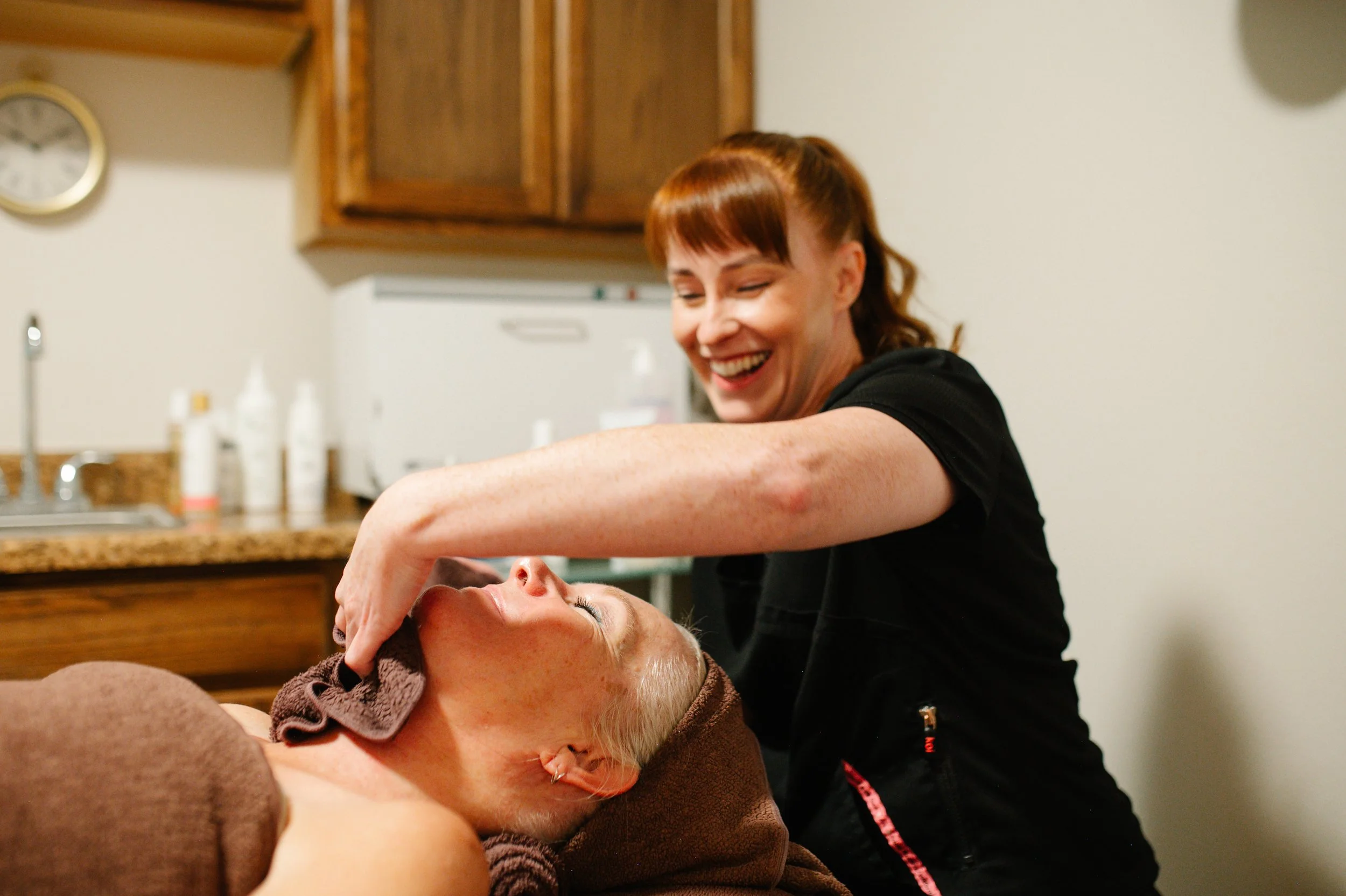 Zoey gently applying a towel to a client’s chin during a facial treatment.