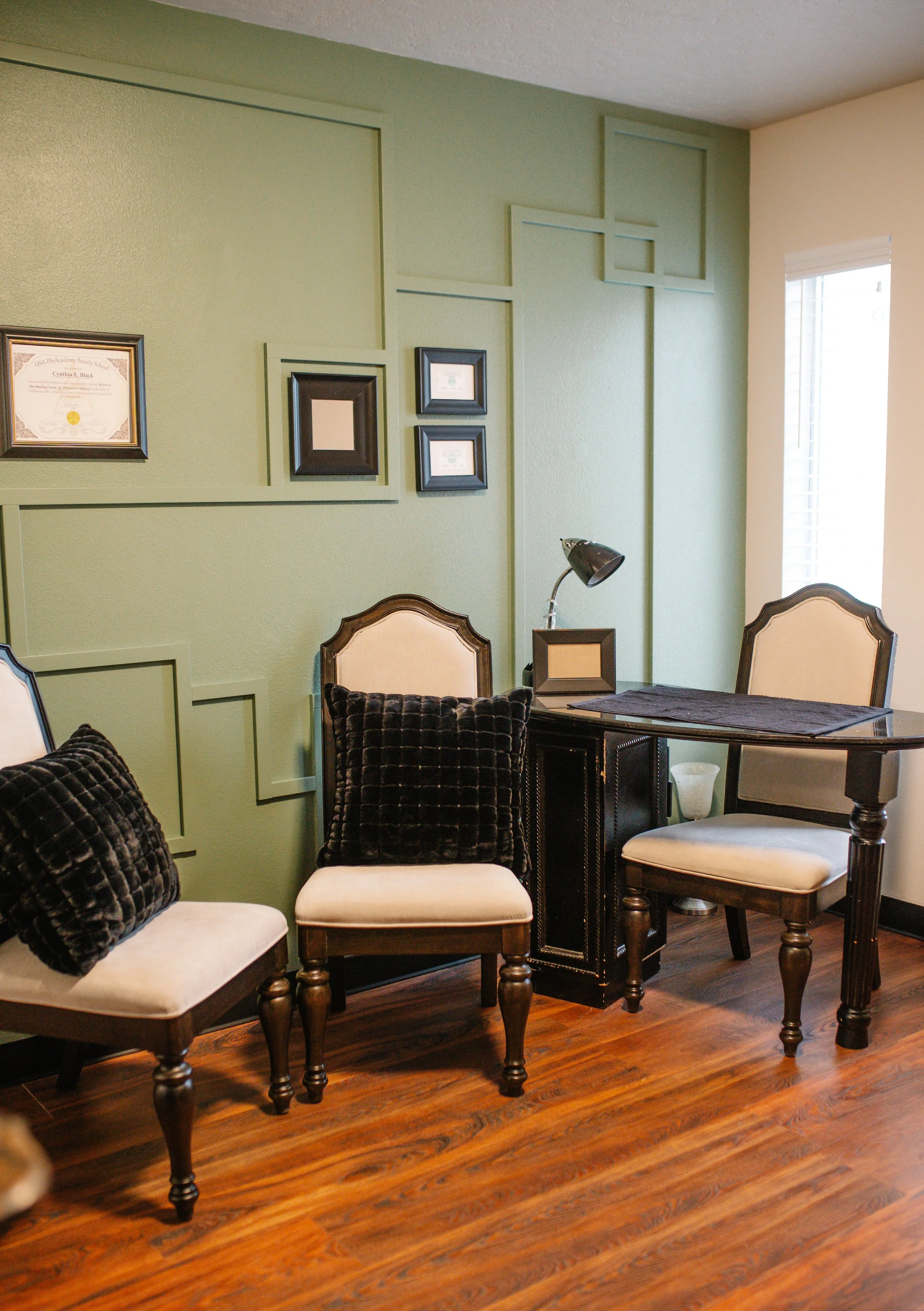 Living room with green and beige walls, framed certificates, and chairs with black velvet cushions and beige seats, wooden floor.