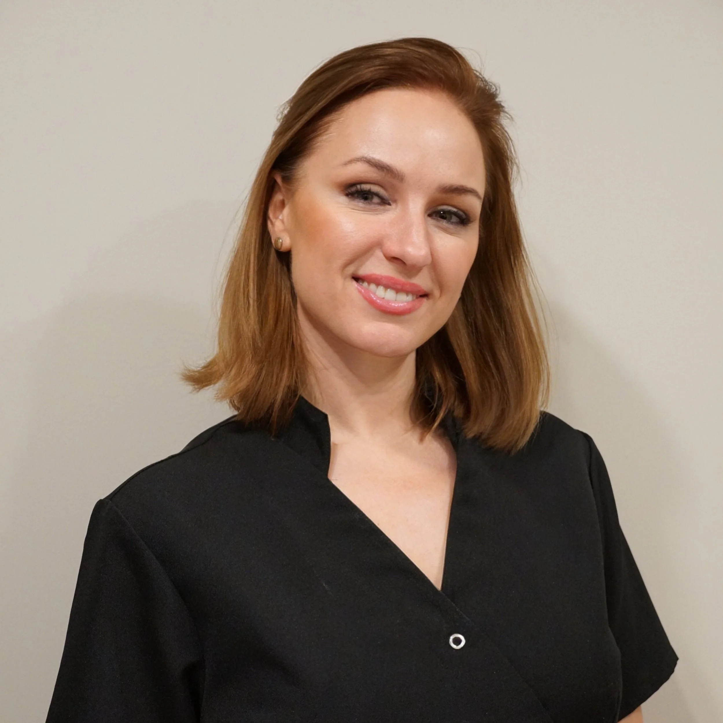 Person in a black uniform smiling in front of a neutral wall.