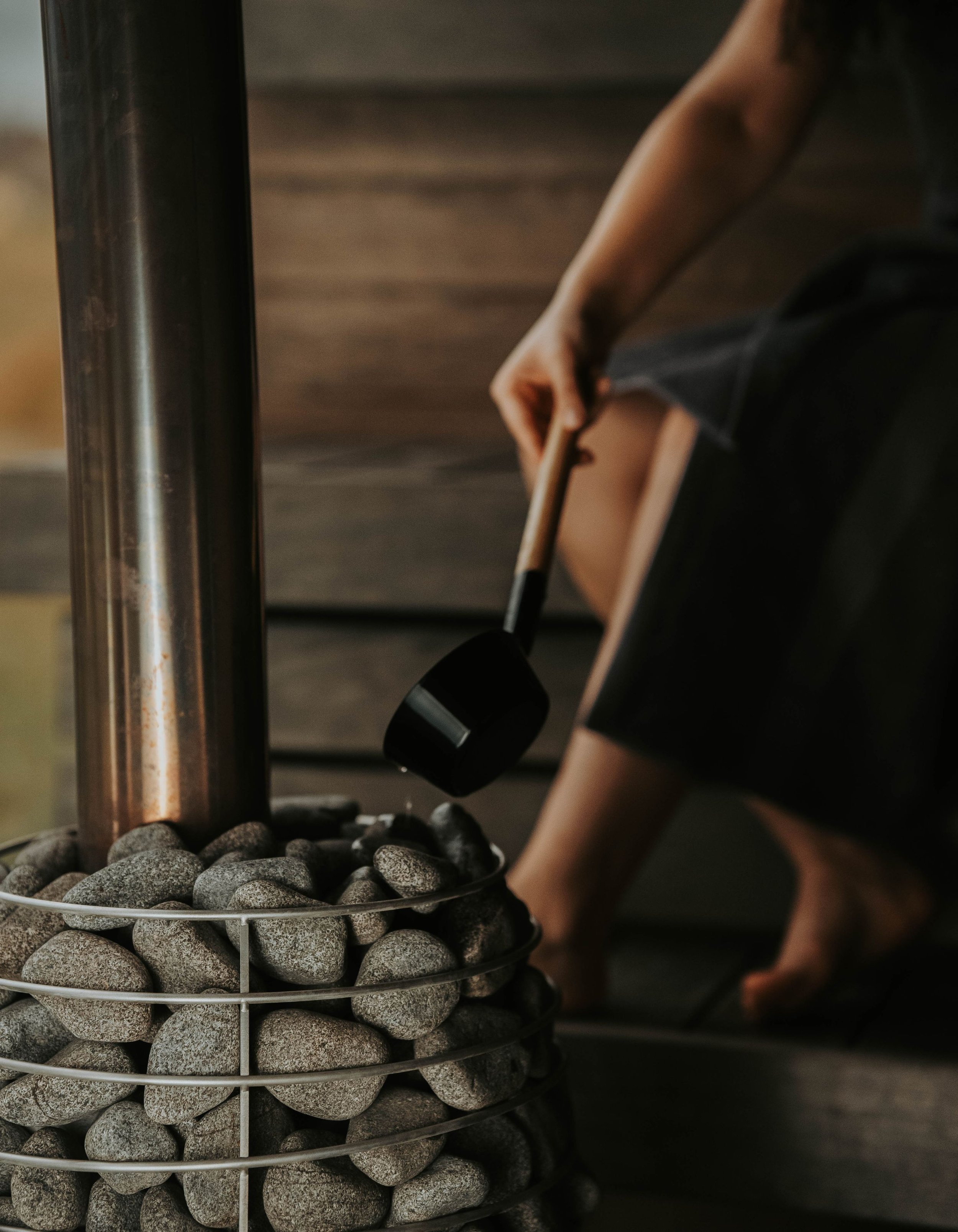 Sauna heater with stones being sprinkled with water by person holding ladle
