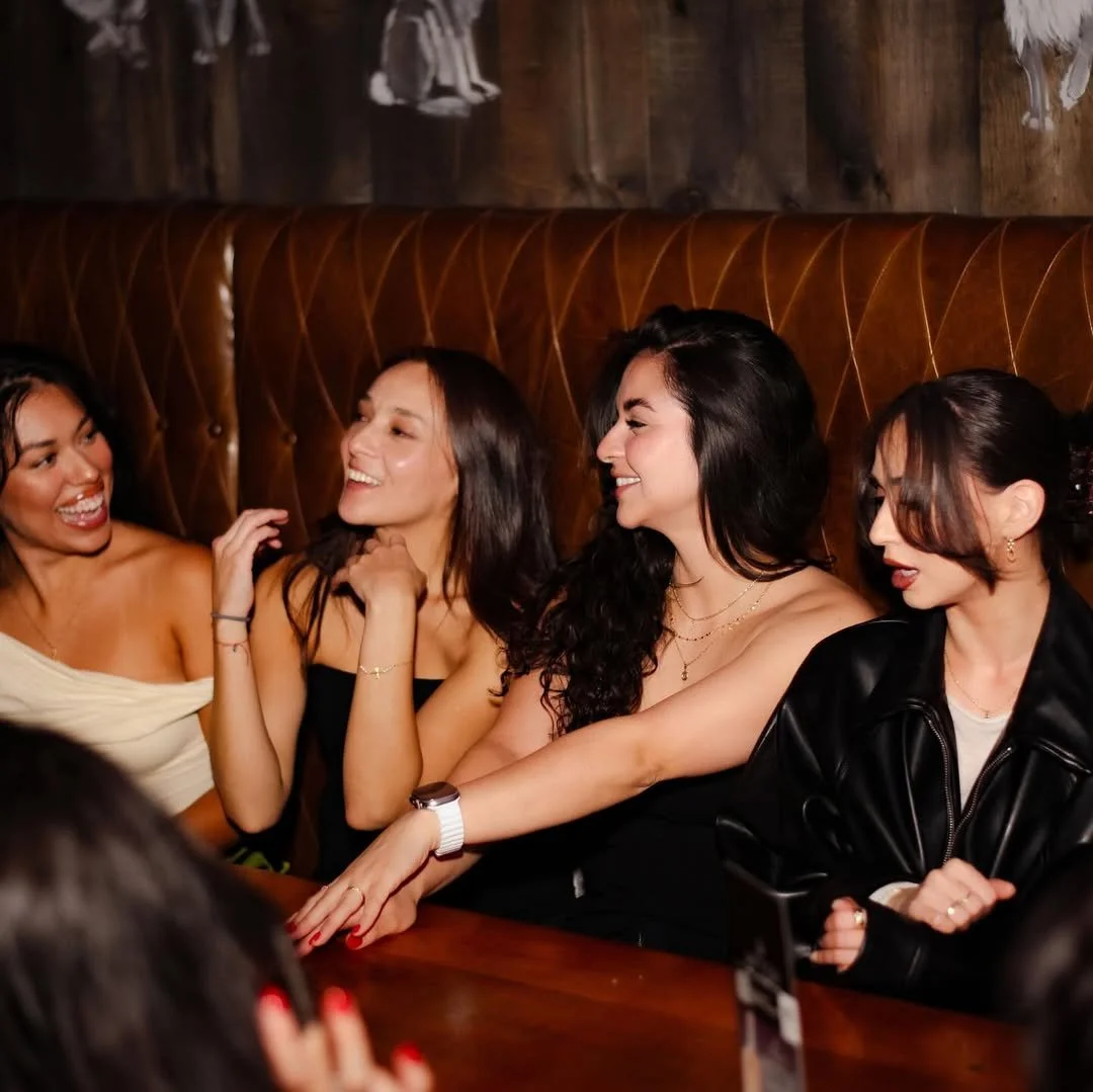 Group of friends laughing and enjoying drinks together inside Fox on John sports bar in Toronto.
