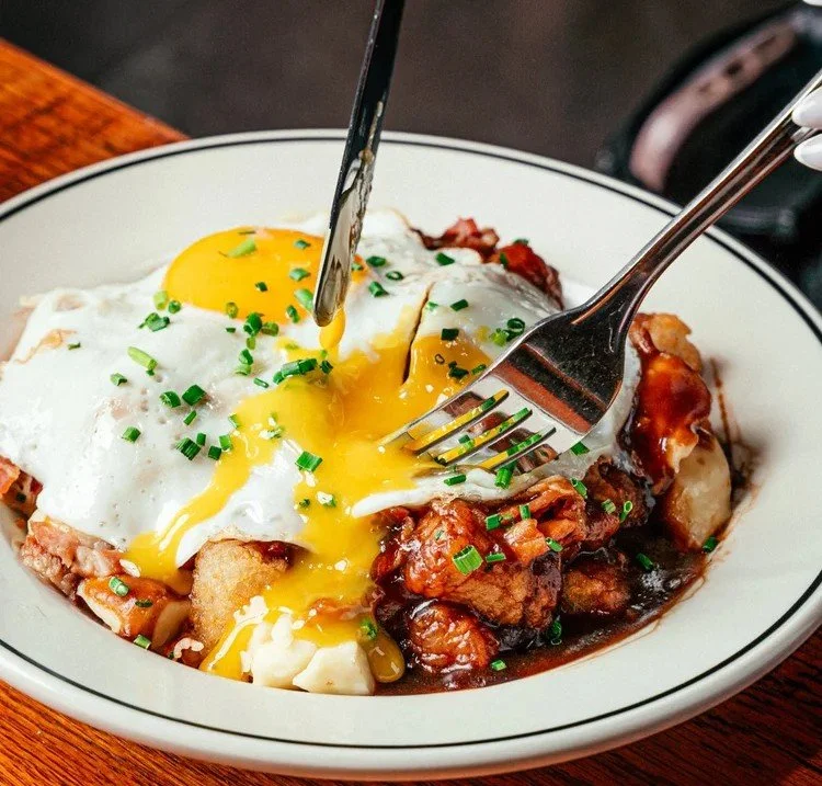 Fox on John brunch dish with crispy potatoes, braised meat, and a runny fried egg being cut at the table.