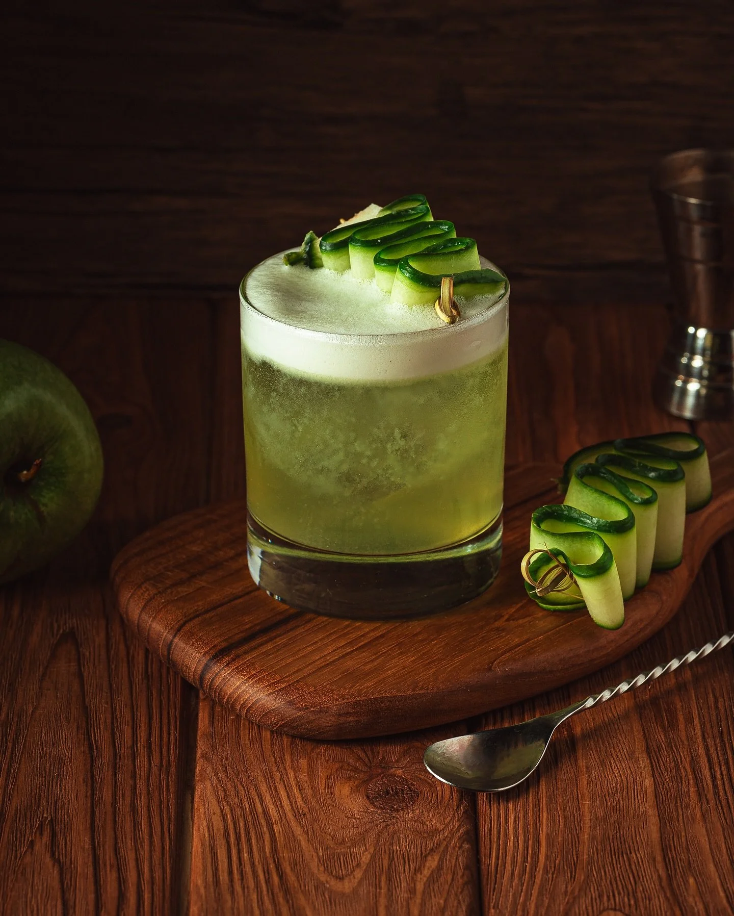 Green cucumber cocktail with frothy top served on a wooden board at Fox on John.