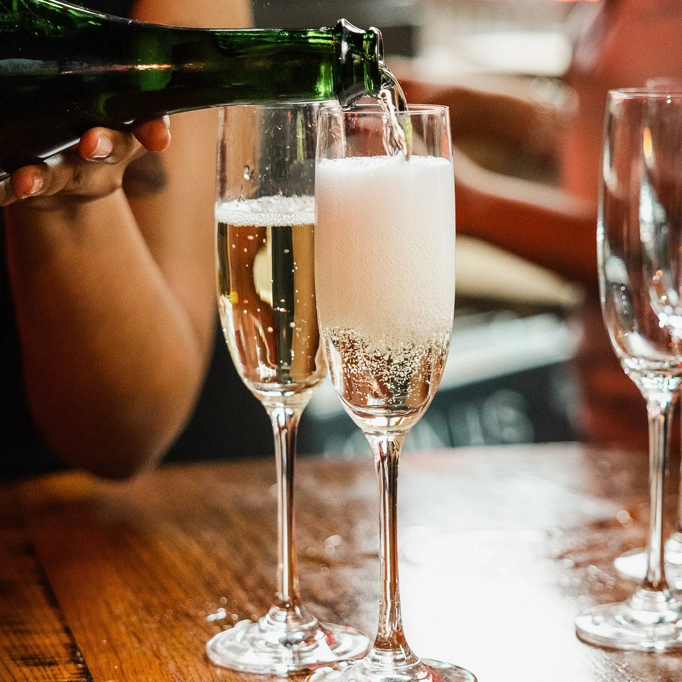 Close up image of Fox on John wine being poured into champagne flute glass kept on a table.