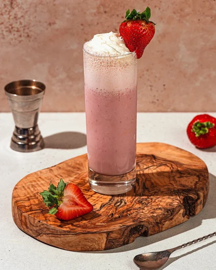 Fox on John strawberry milkshake-style cocktail topped with whipped cream, served on a wooden board.