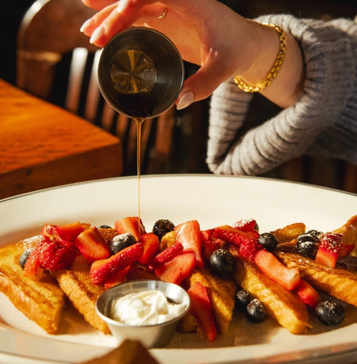 Fox on John brunch waffle topped with fresh berries, cream, and syrup being poured tableside.