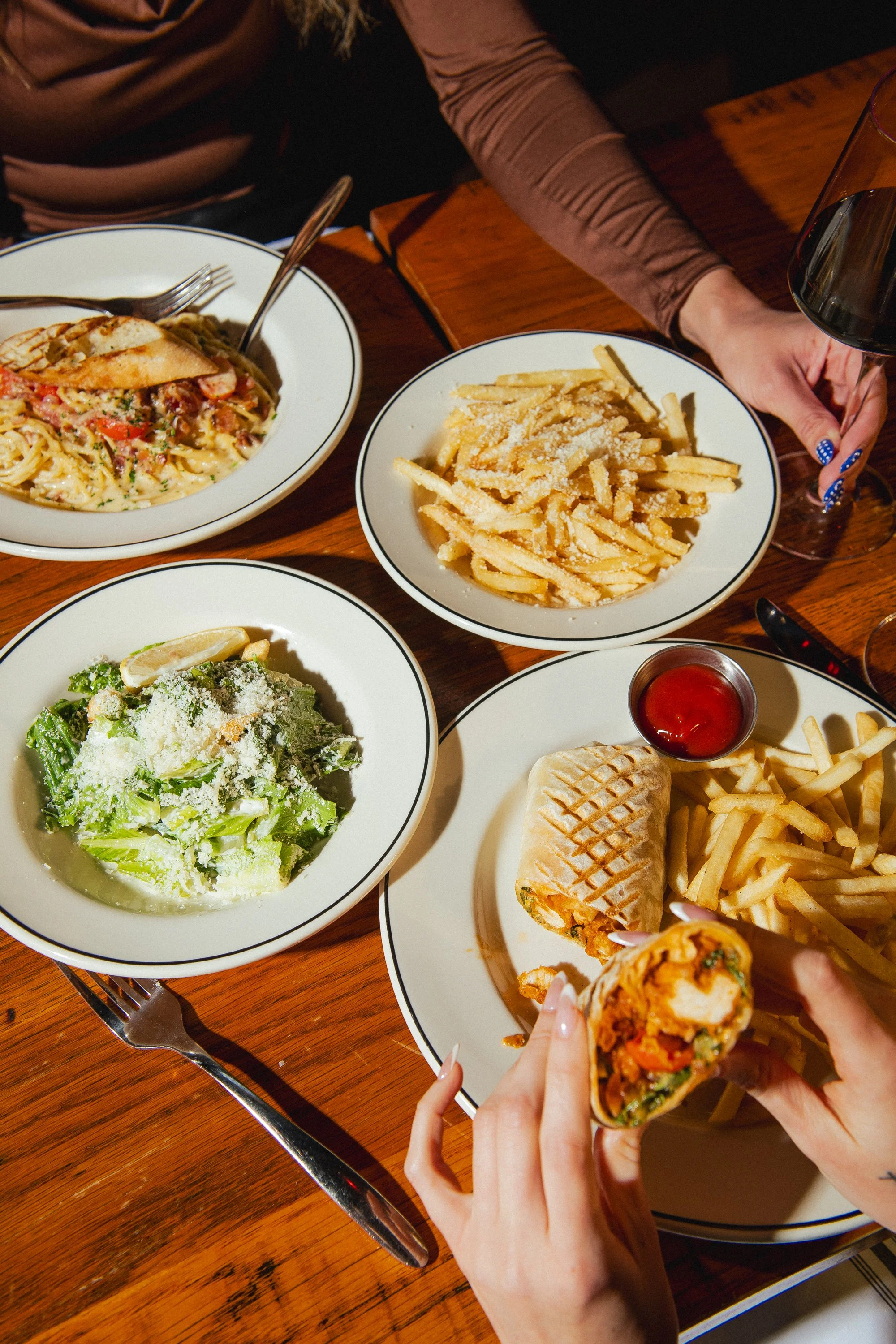 Plates of pasta, fries, salad, and wraps arranged on a dining table at Fox on John restaurant.