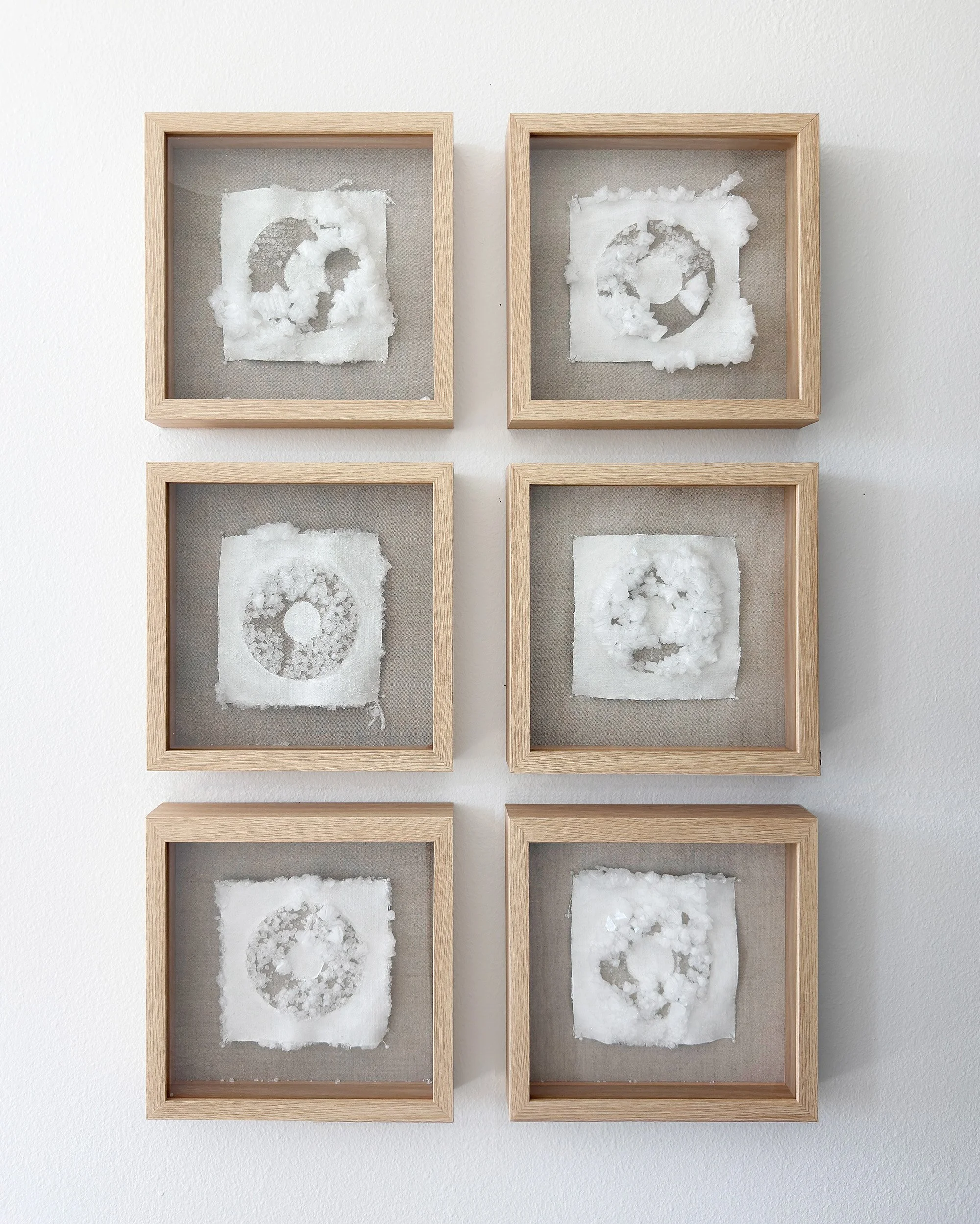 A series of six framed textile artworks featuring crystals grown on Belgian linen