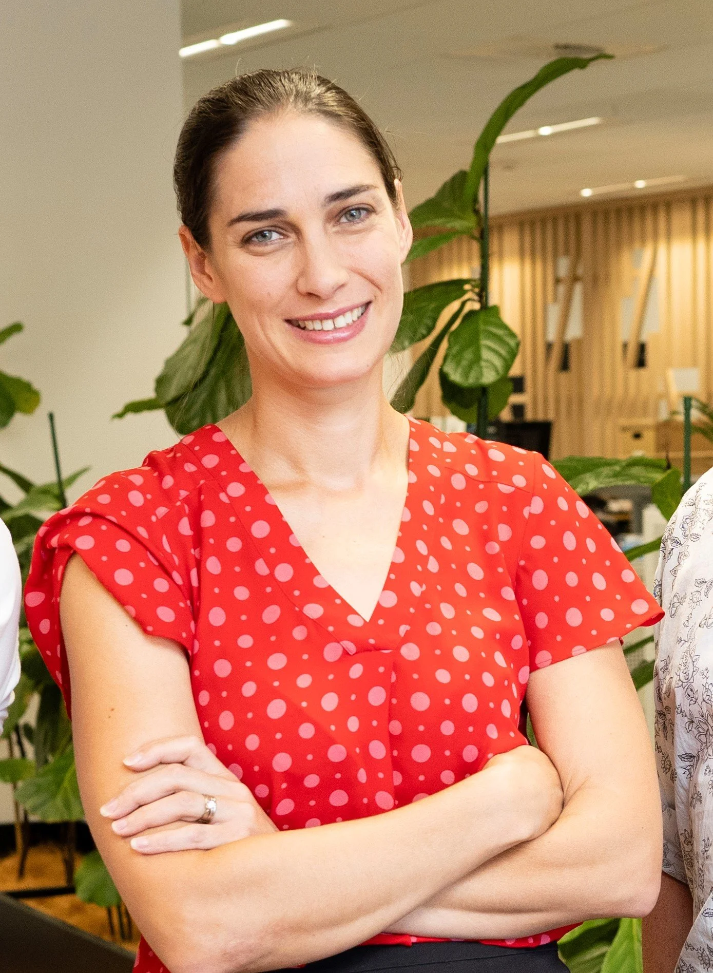 Man in a light blue shirt with arms crossed, smiling, standing indoors with wooden decor and a plant in the background.
