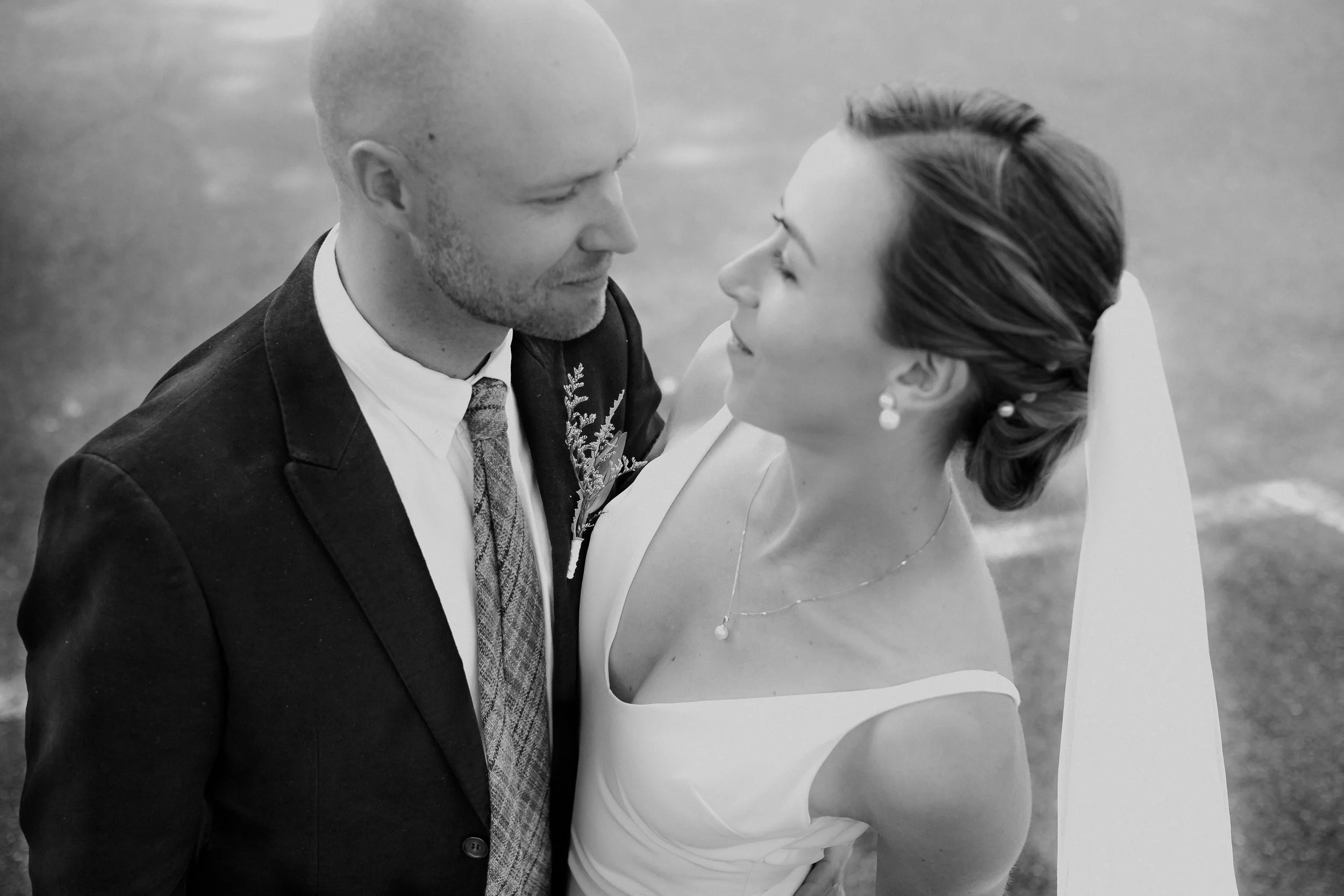 A black and white photo of a bride and groom standing close, looking into each other's eyes on their wedding day.
