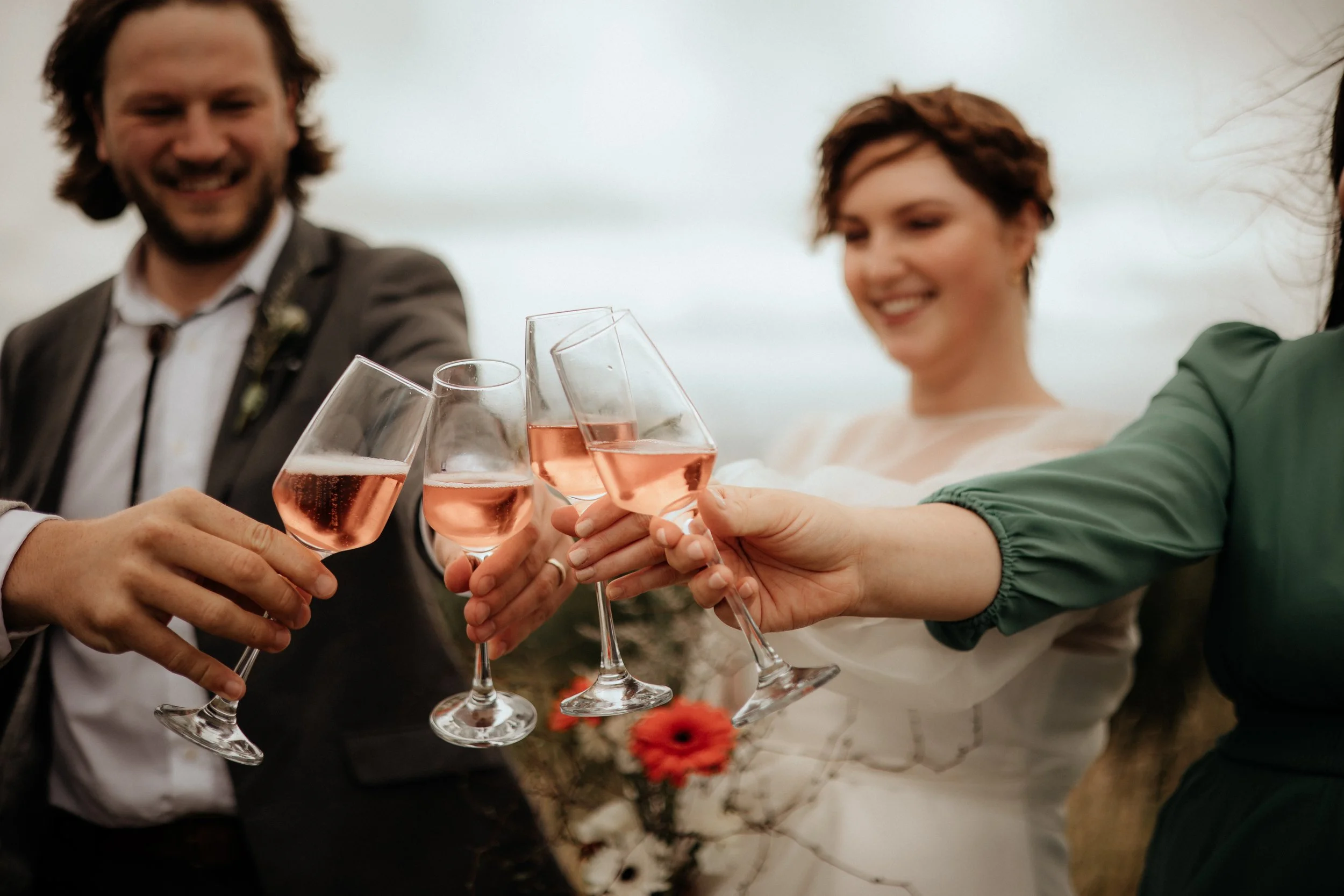 Couple celebrating with friends, clinking glasses of rosé wine outdoors at a wedding or celebration, smiling and enjoying the moment.