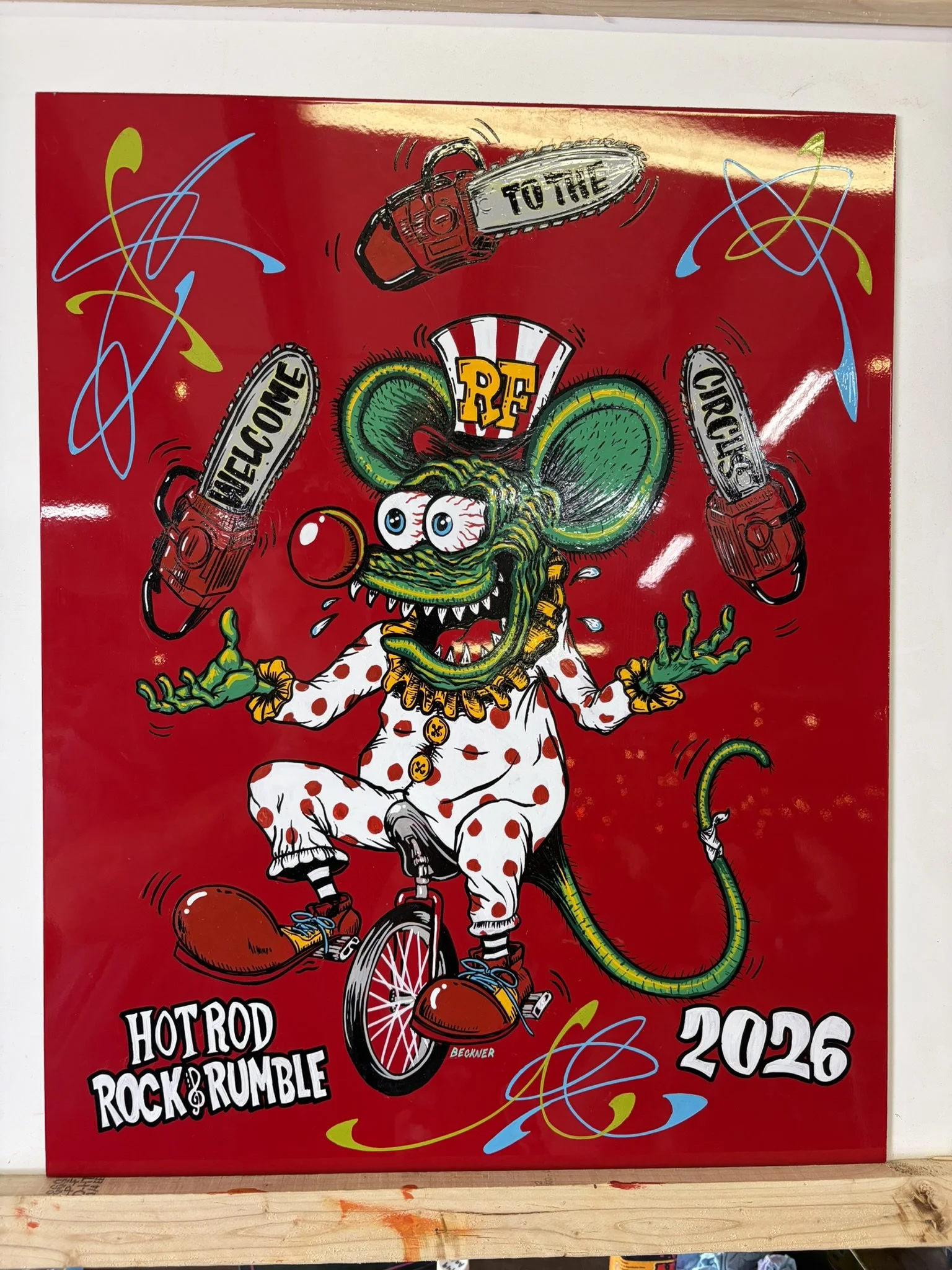 Red art panel with a hand painted illustration of Rat Fink riding a unicycle, juggling chain saws. Panel is for the 2026 Hot Rod Rock & Rumble. Painted by Matt Beckner