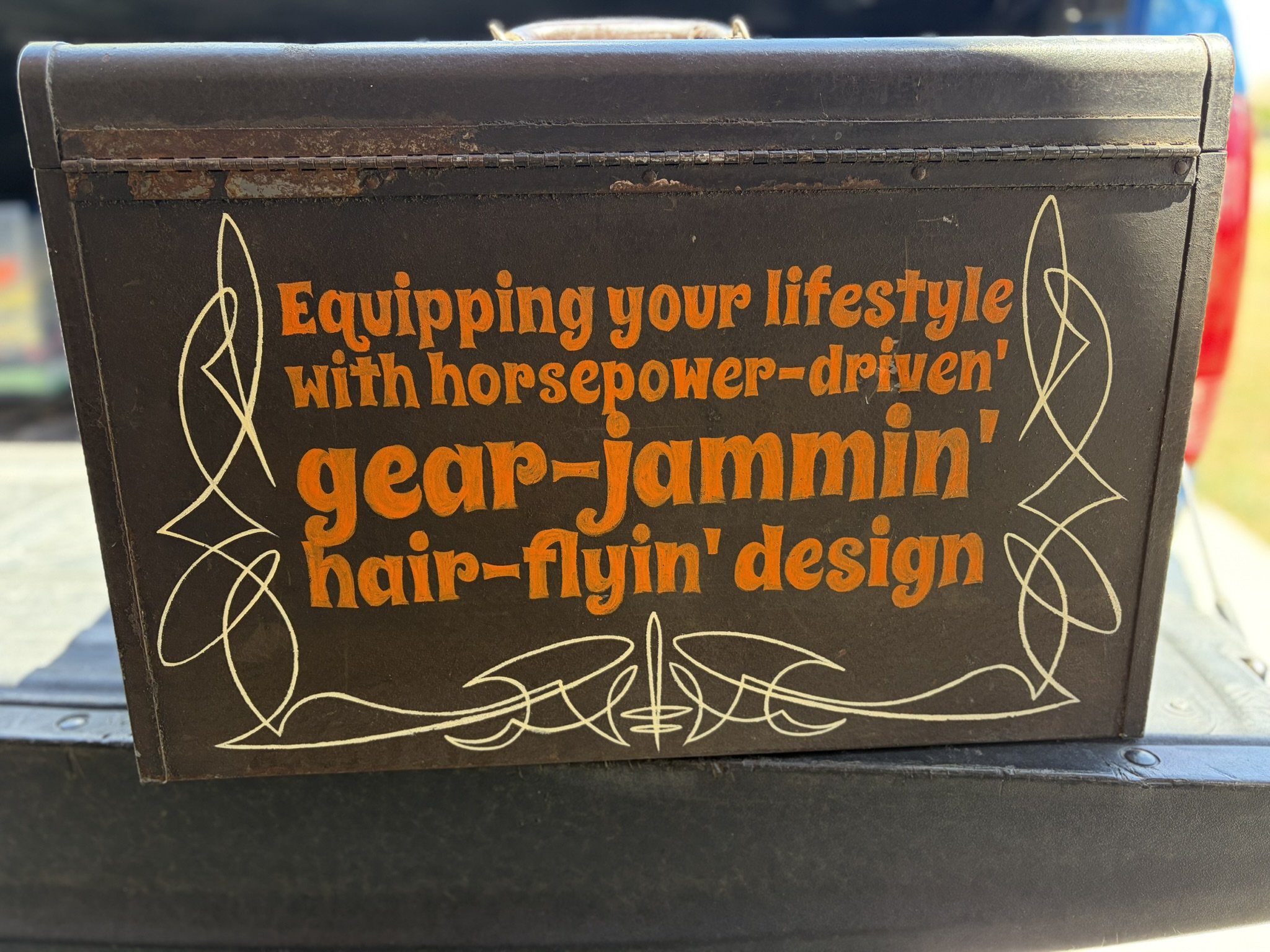Hand lettered in orange: "Equipping your lifestyle with horsepower-driven', gear jammin', hair-flyin' design" with ivory pinstriping all on the back of a toolbox by Matt Beckner