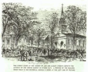 An old print showing the street scene at the corner of Ann and Albany Streets in Little Falls, depicting the activities of the Cheese Market in bygone days. A portion of the building which today is the Little Falls Historical Society is visible at the left side of the picture.