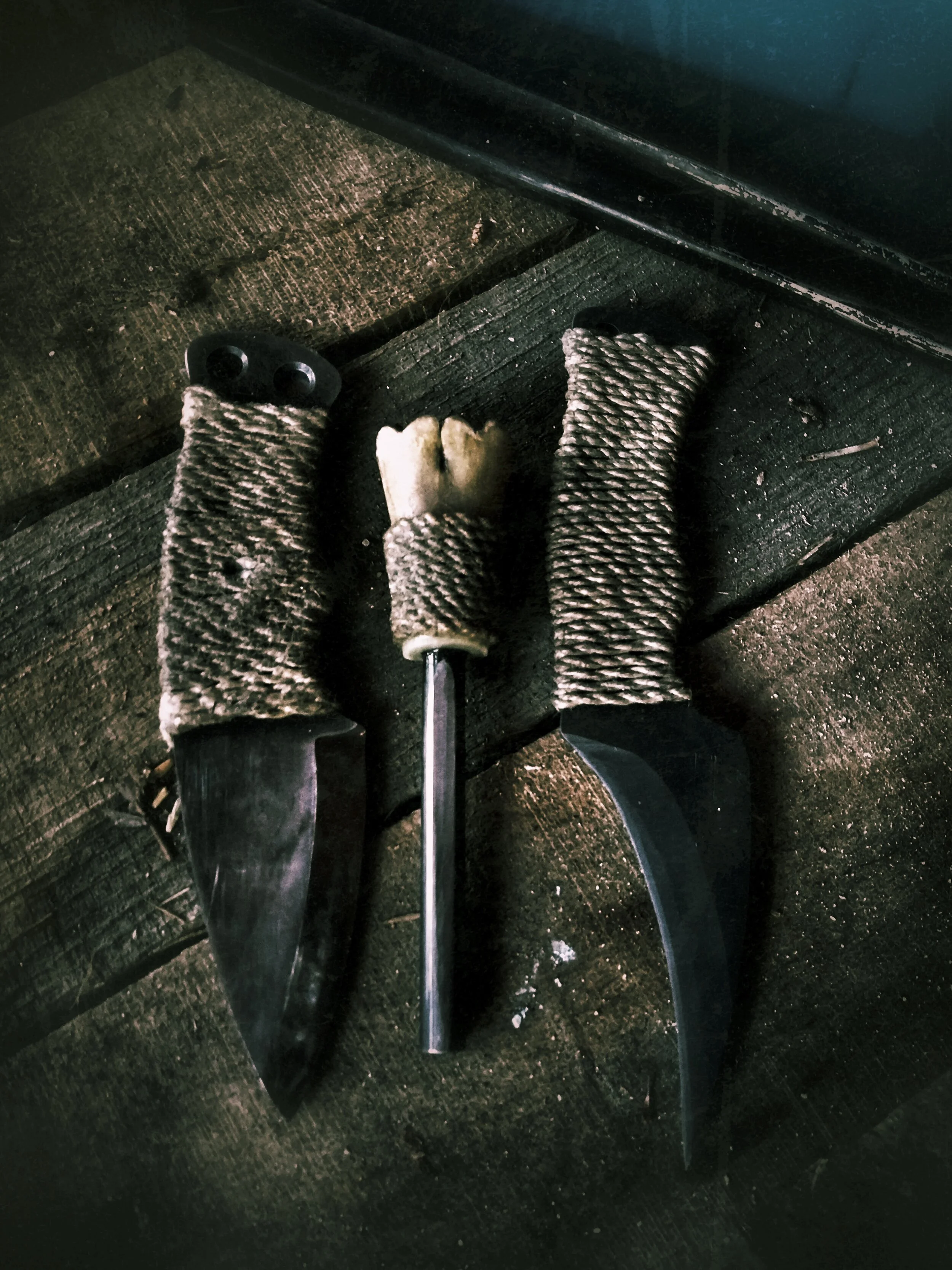 Two wrapped-handle knives laying to either side of a bone-handled fire-starter.