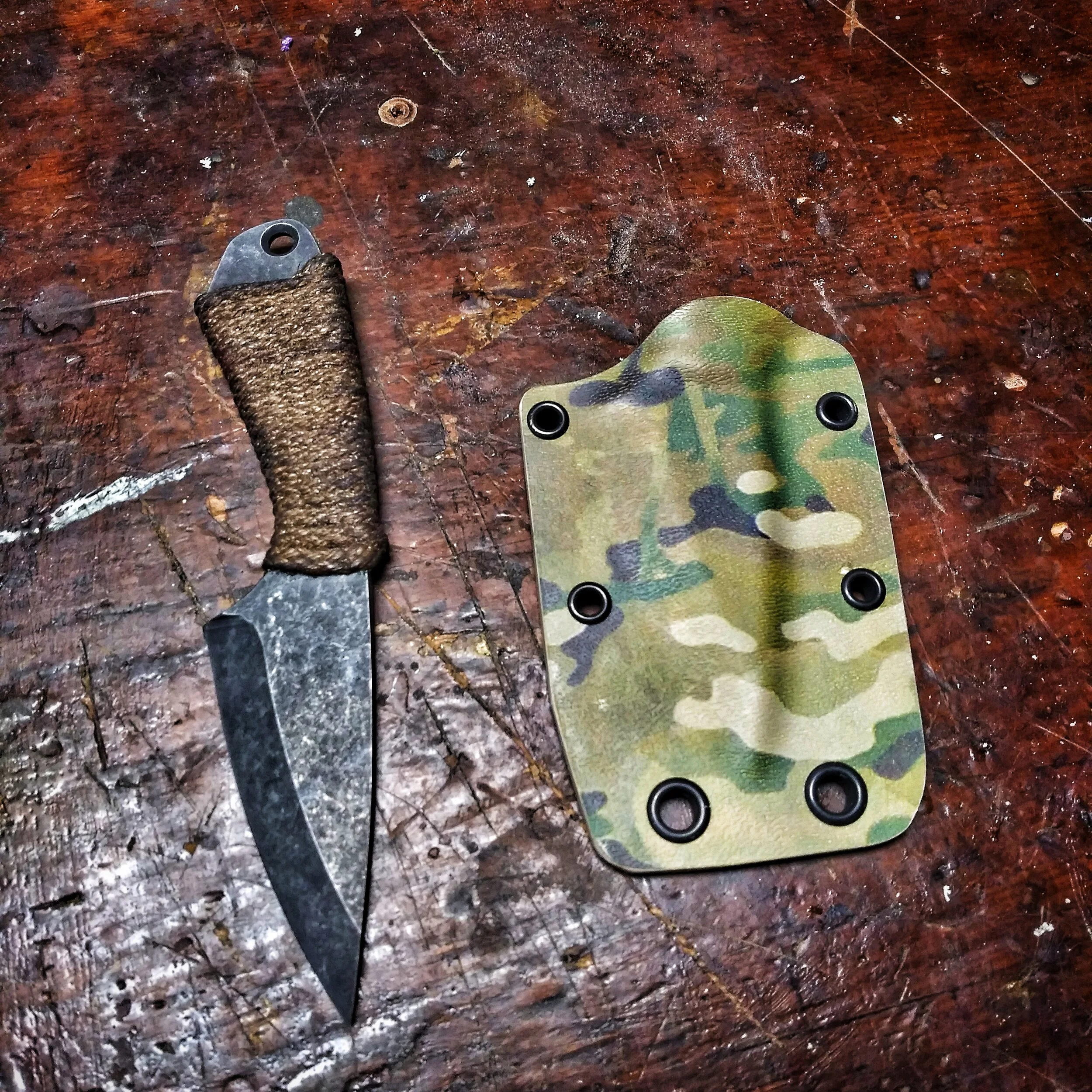 A knife resting beside its sheath on a wooden surface.
